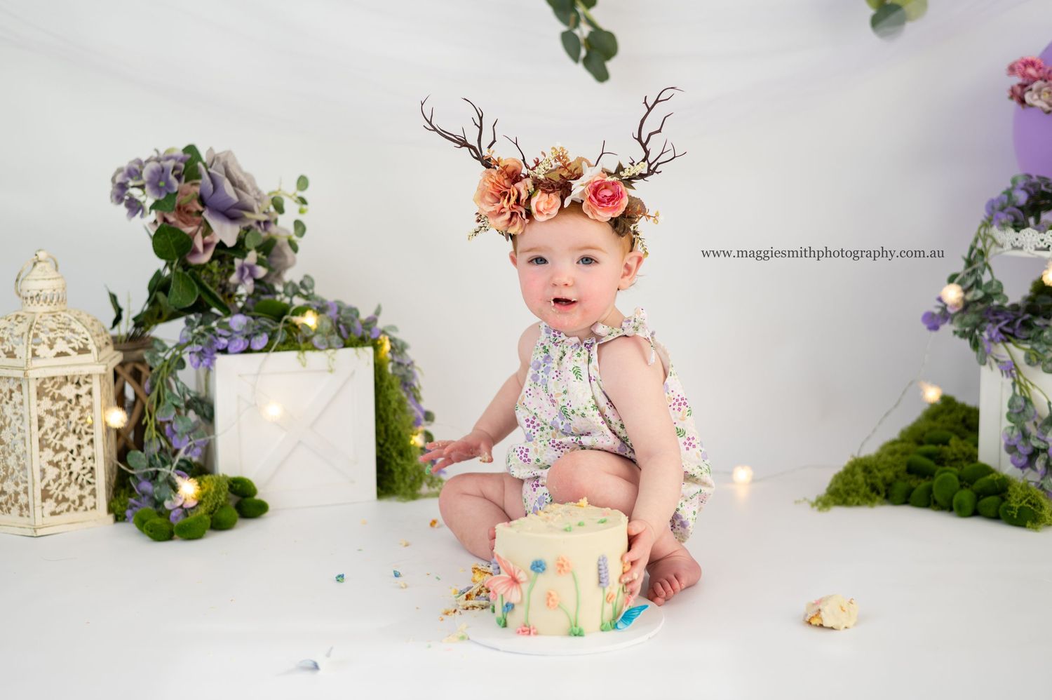 Whimsical fairy cake smash shoot of a baby wearing a floral crown near a decorated cake with fairy-style decorative elements.