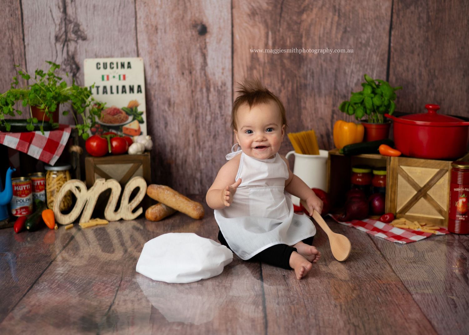 Kitchen themed photo setup with wooden backdrop, chef's hat, red cookware, and rustic decorative elements. Spaghetti smash.