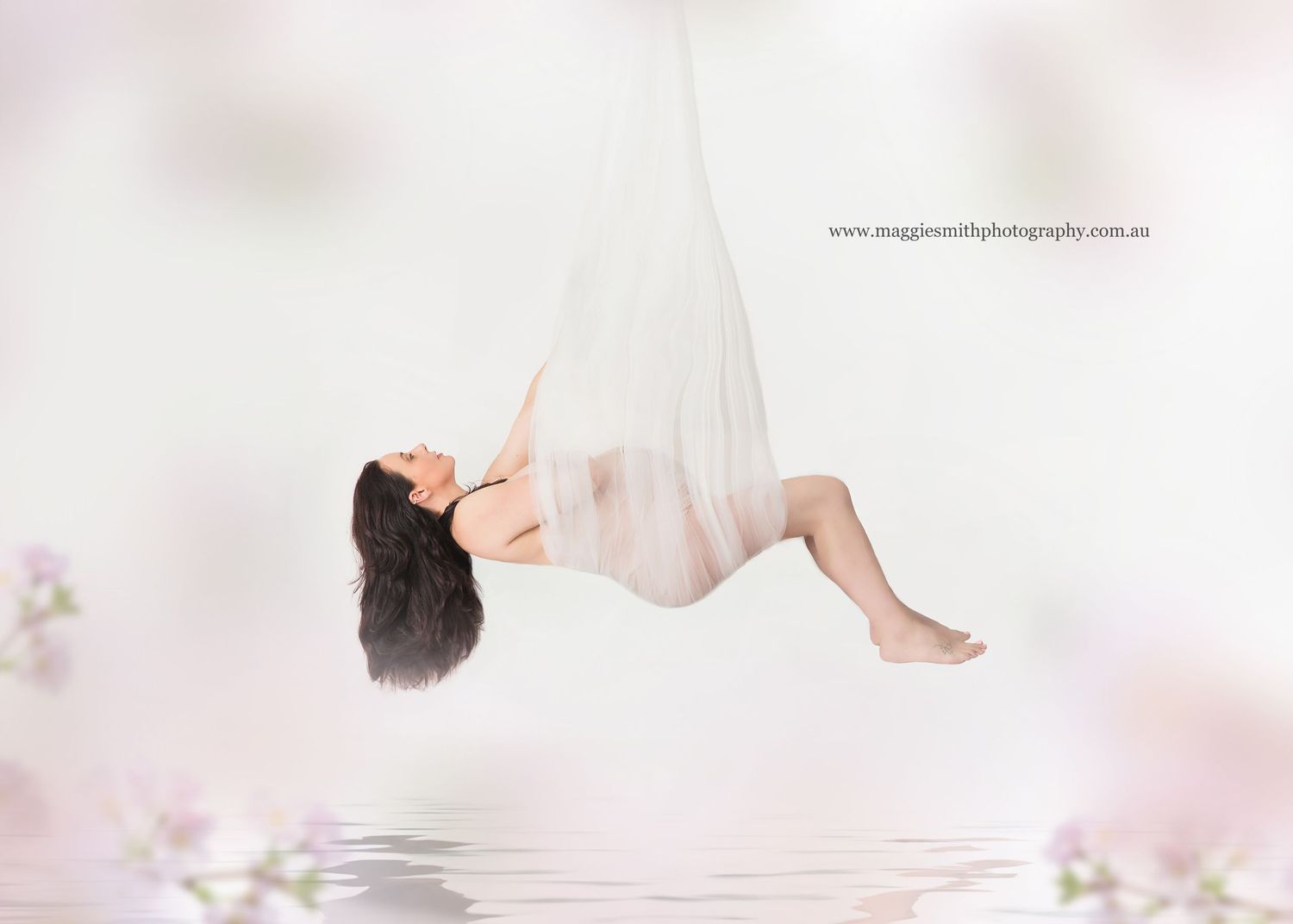 Ethereal artistic photo of maternity image of a floating pregnant woman in soft pink atmosphere above reflective water surface.