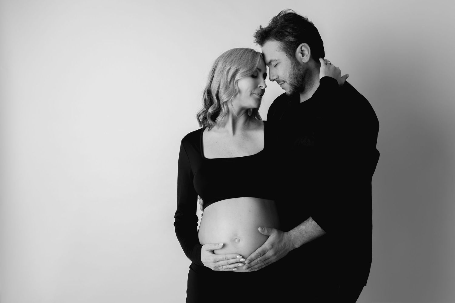 A romantic black and white photo series showing intimate maternity moments between a couple embracing in low light. Maternity shoot
