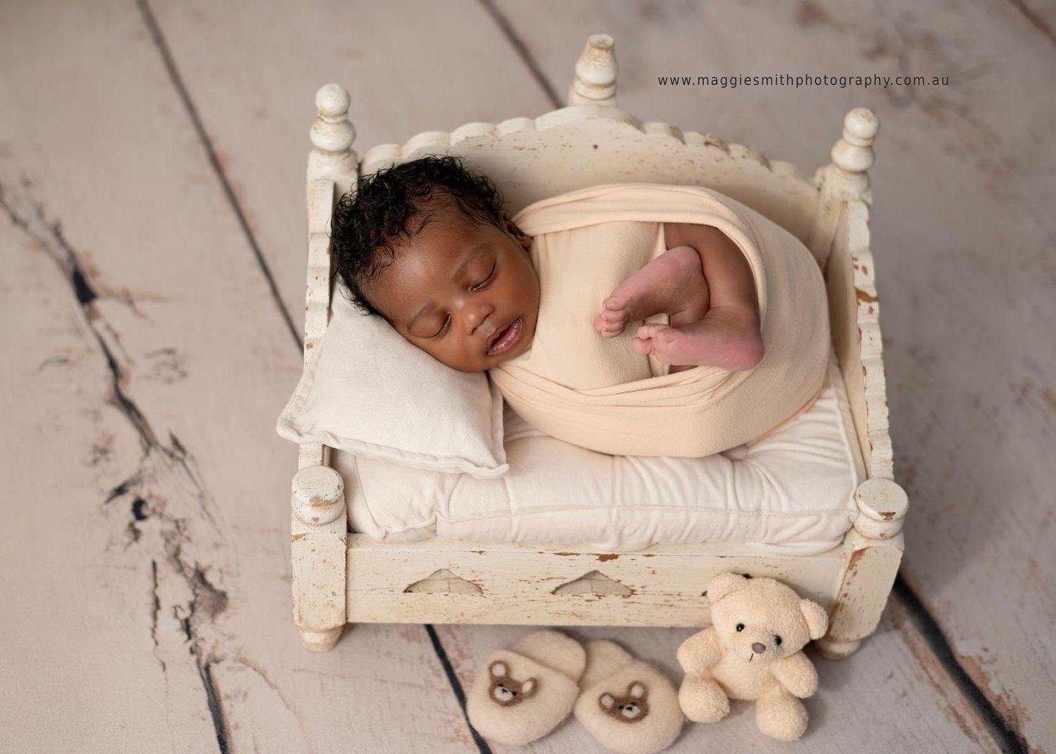 Sleeping newborn baby rests peacefully on white vintage bed prop in professional photography studio setting.