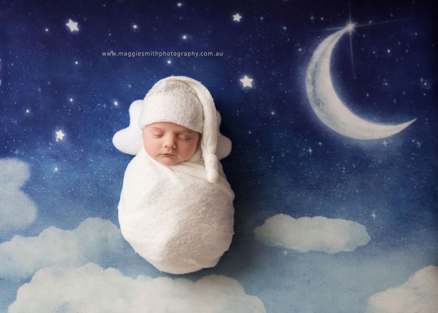 A sleeping newborn wrapped in white cloth floats dreamily against a starry night sky backdrop with a crescent moon.