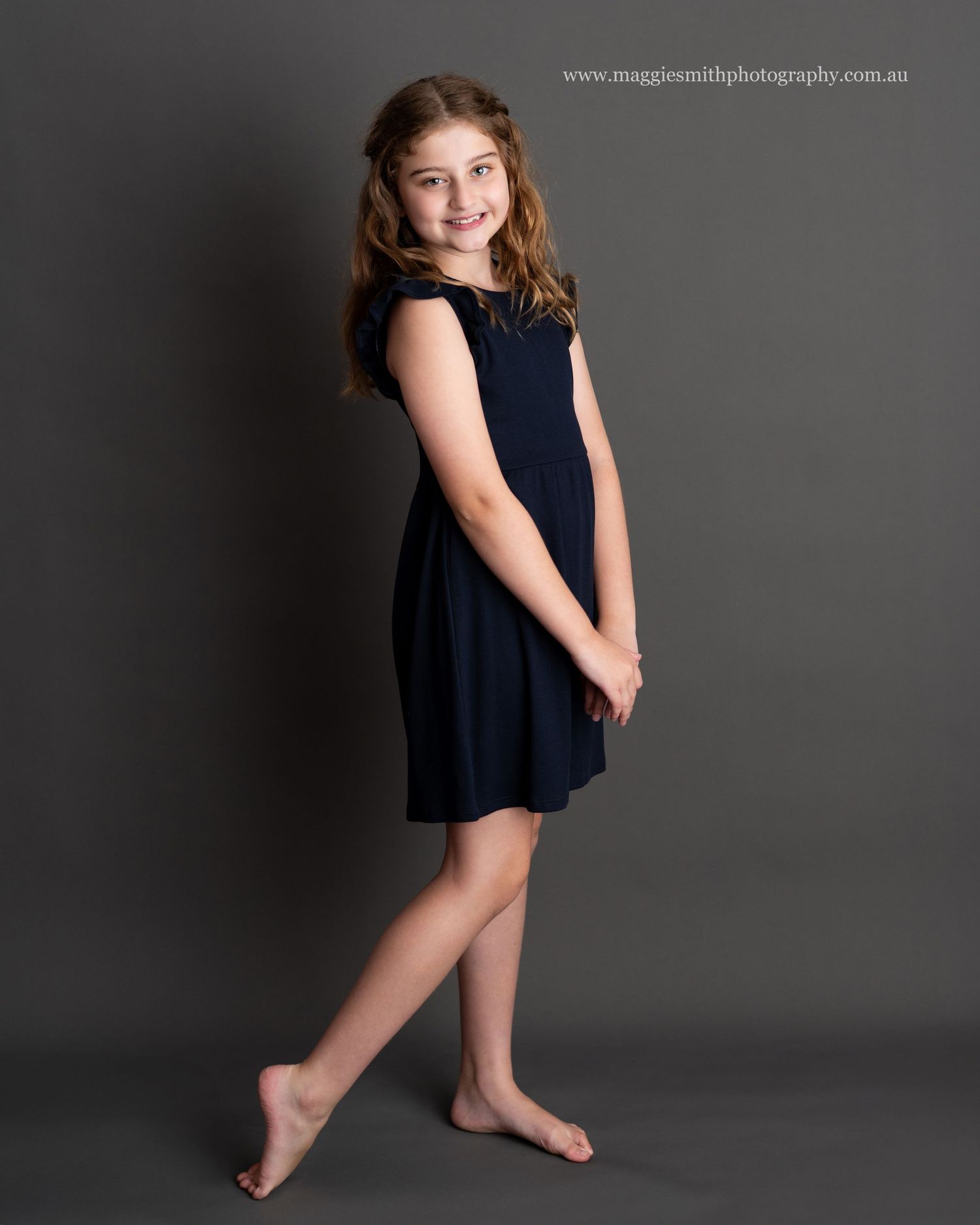 Young actress in a navy blue dress poses gracefully against a dark background for a portrait photo. Headshot photography