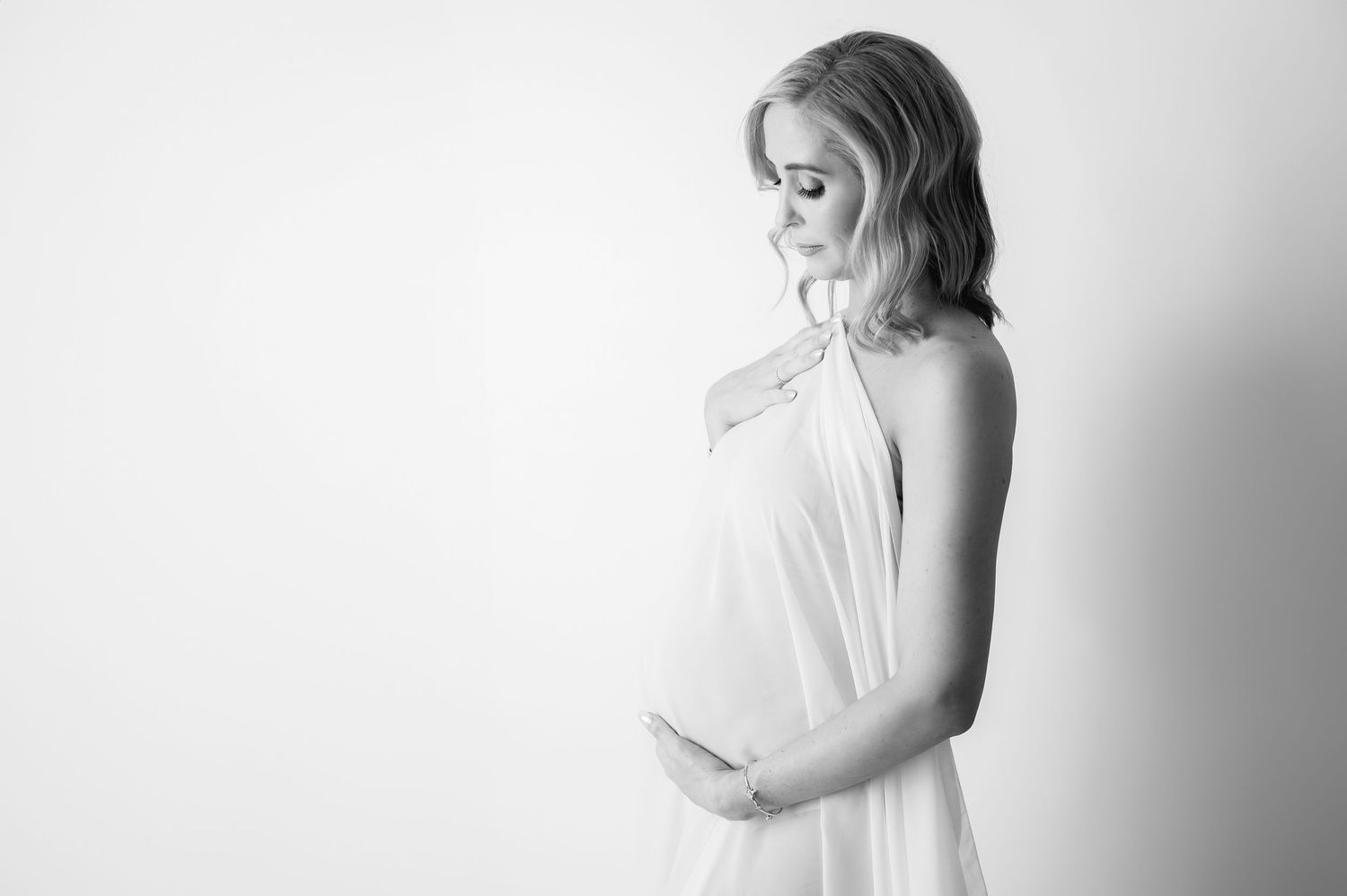 A minimalist black and white maternity photography series showing a pregnant woman in flowing white fabric.