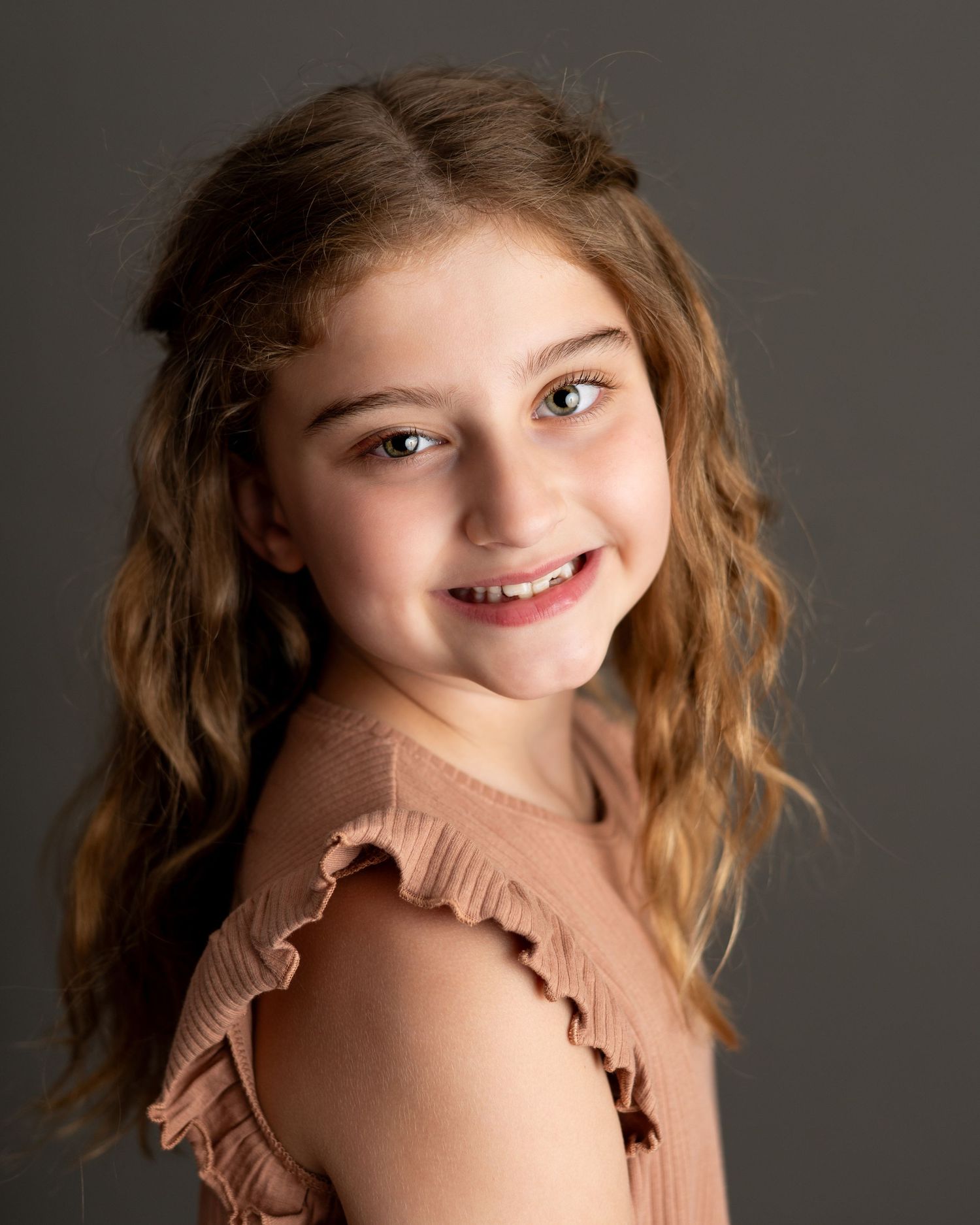 Portrait series showing warm expressions and soft lighting against dark background in pink sweater. Headshot photography, kids portfolio