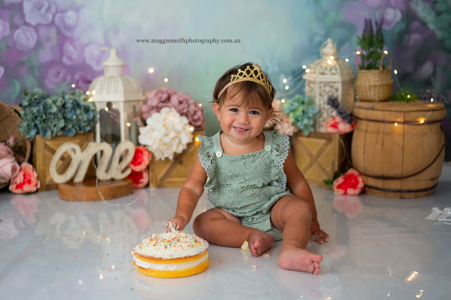 First birthday celebration setup with lanterns, wooden barrels, floral decorations, and a cake against a dreamy background.