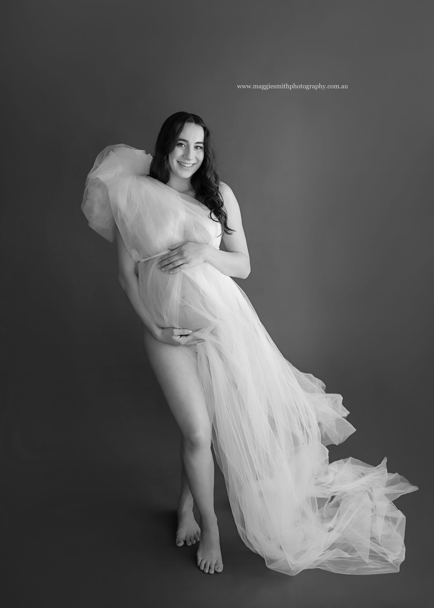 Artistic black and white maternity portrait with flowing white tulle fabric draping around an expectant mother.
