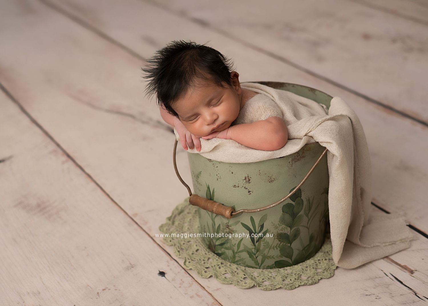A newborn baby sleeps peacefully on a light wooden floor while being photographed from different angles.