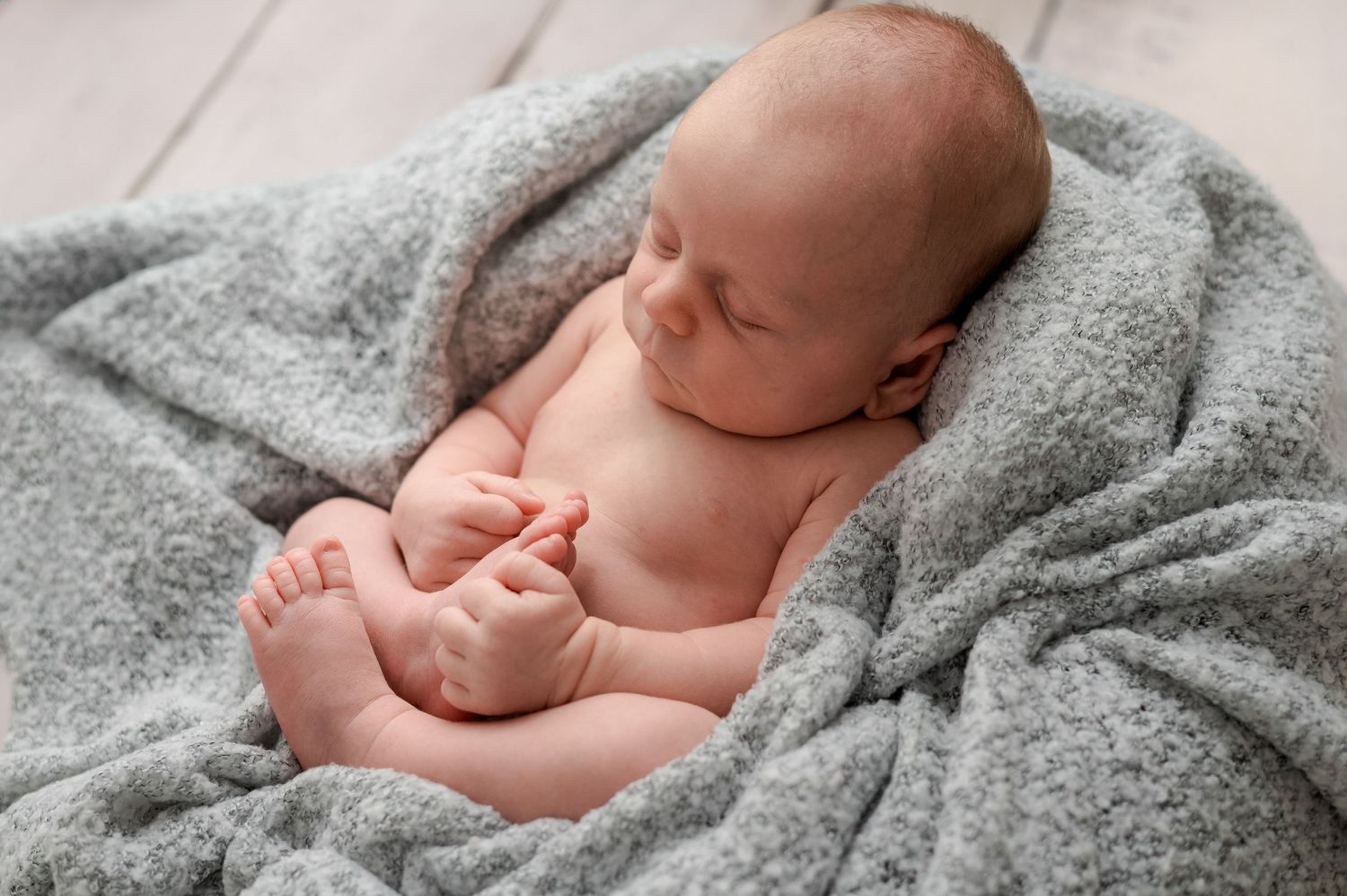 A sleeping newborn baby swaddled in soft gray blankets on a textured background.