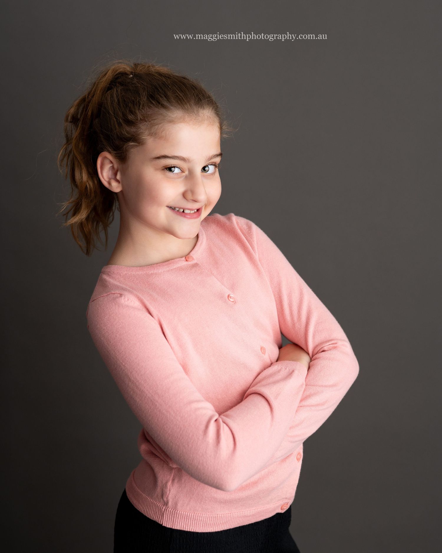 Young person in a pink sweater poses against dark background with ponytail hairstyle and casual style. Headshot photography