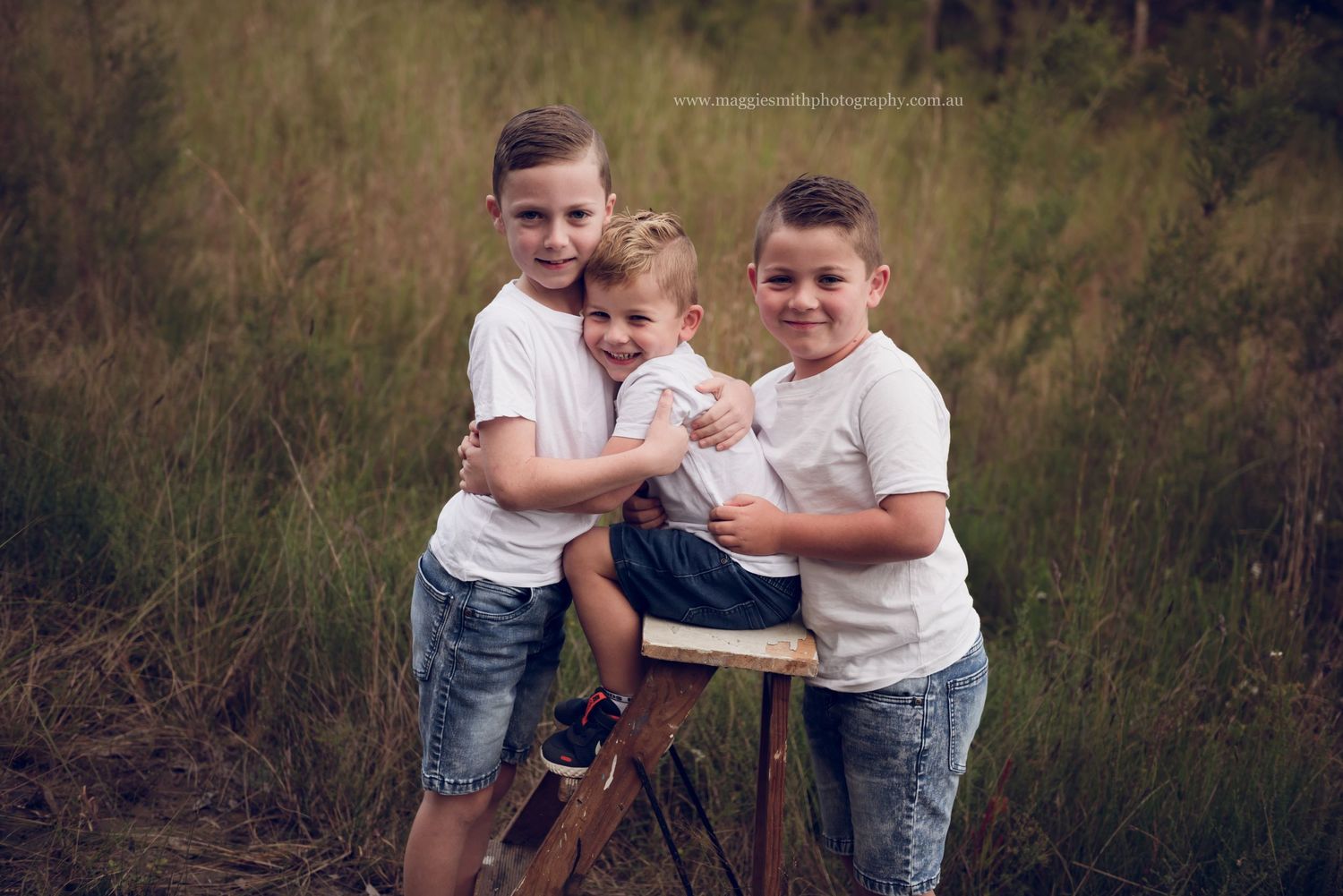Two young boys play and laugh together in a grassy outdoor setting during golden hour.