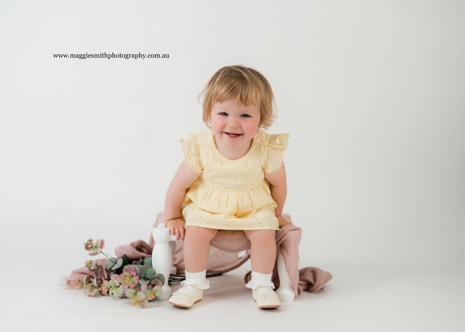 A child in a yellow dress sits and smiles on a white studio backdrop in a series of connected photos.