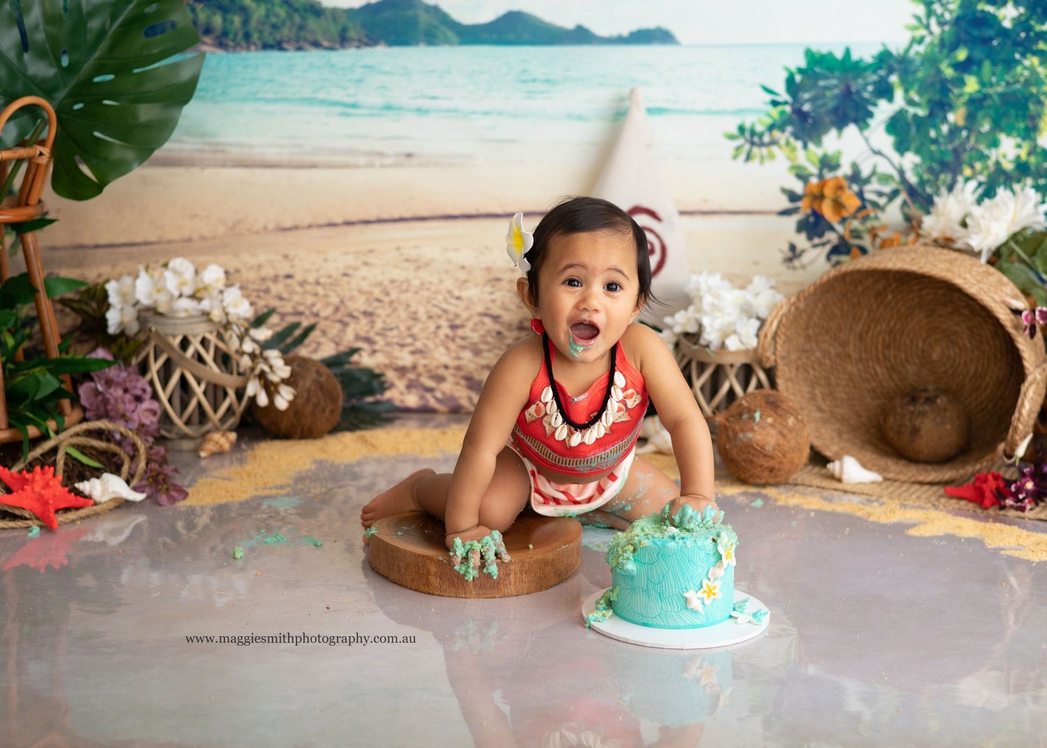 Moana themed cake smash on a tropical beach backdrop with cake and festive decorations.