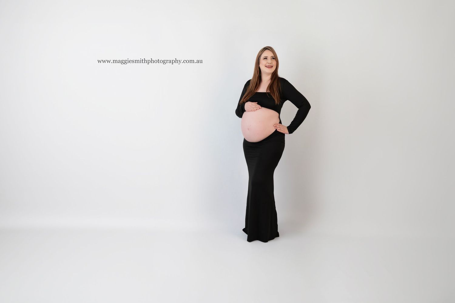 An expectant mother in a black crop top and fitted skirt poses elegantly against a white studio background.