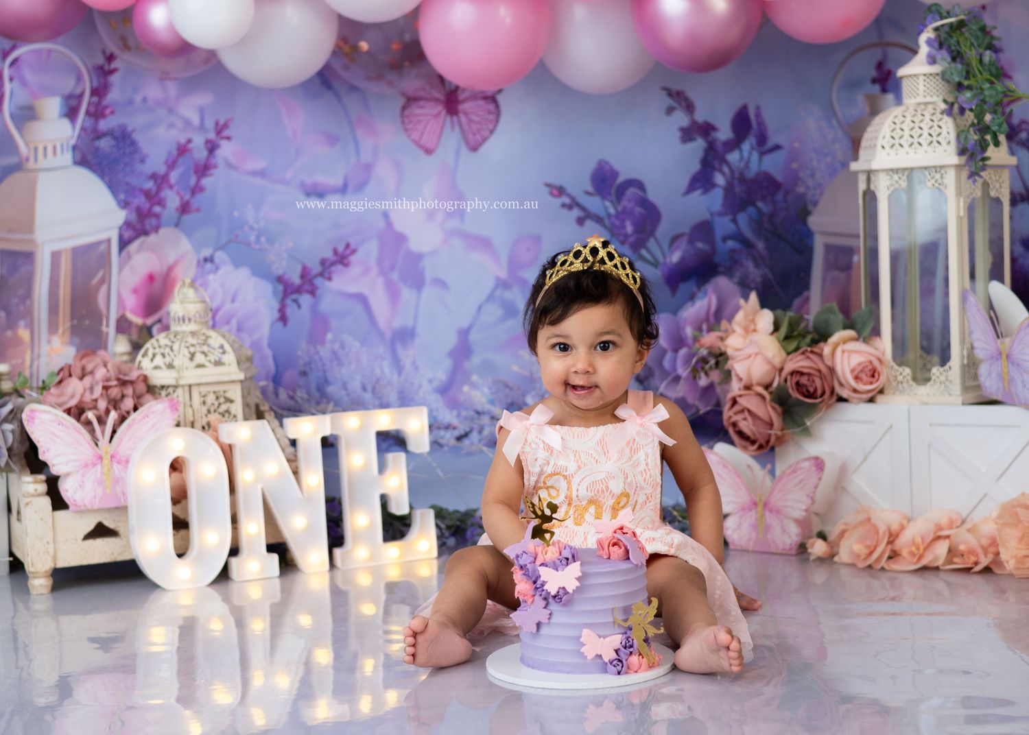 First birthday celebration setup with floral backdrop in purple and pink tones. Cake smash photography