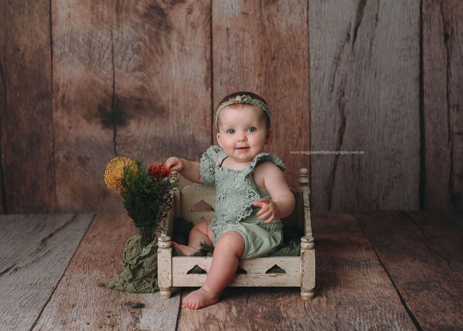 A small child sitting in a rustic wooden crate with orange flowers against a wooden wall backdrop.