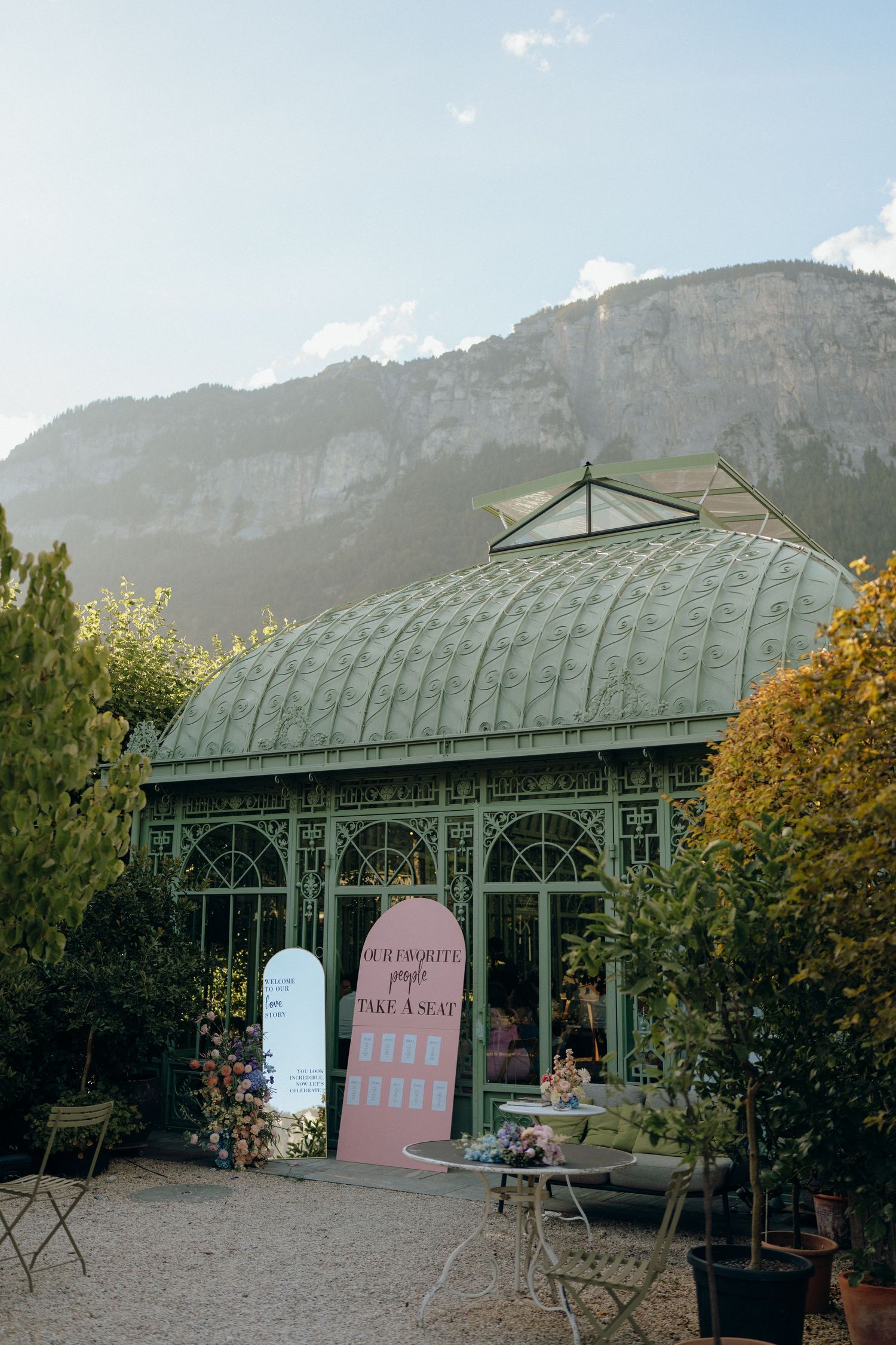 Stunning green Victorian greenhouse wedding venue with arched glass roof and mountain backdrop at golden hour.