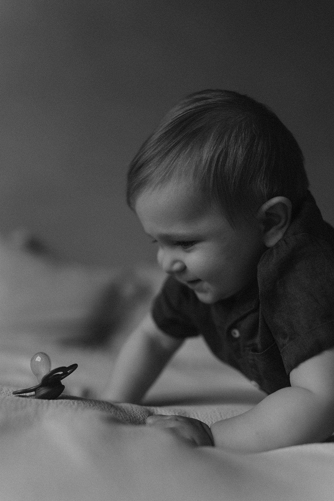 Black and white photo of a young toddler lying down and looking at a pacifier.