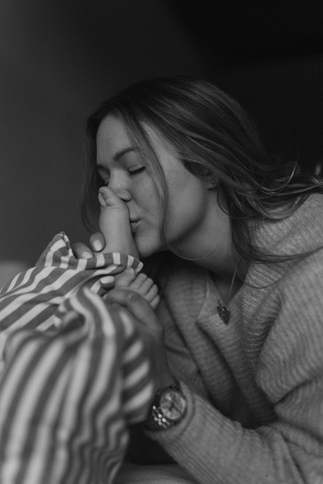 Black and white photo of a mother lovingly kissing her babys tiny foot.