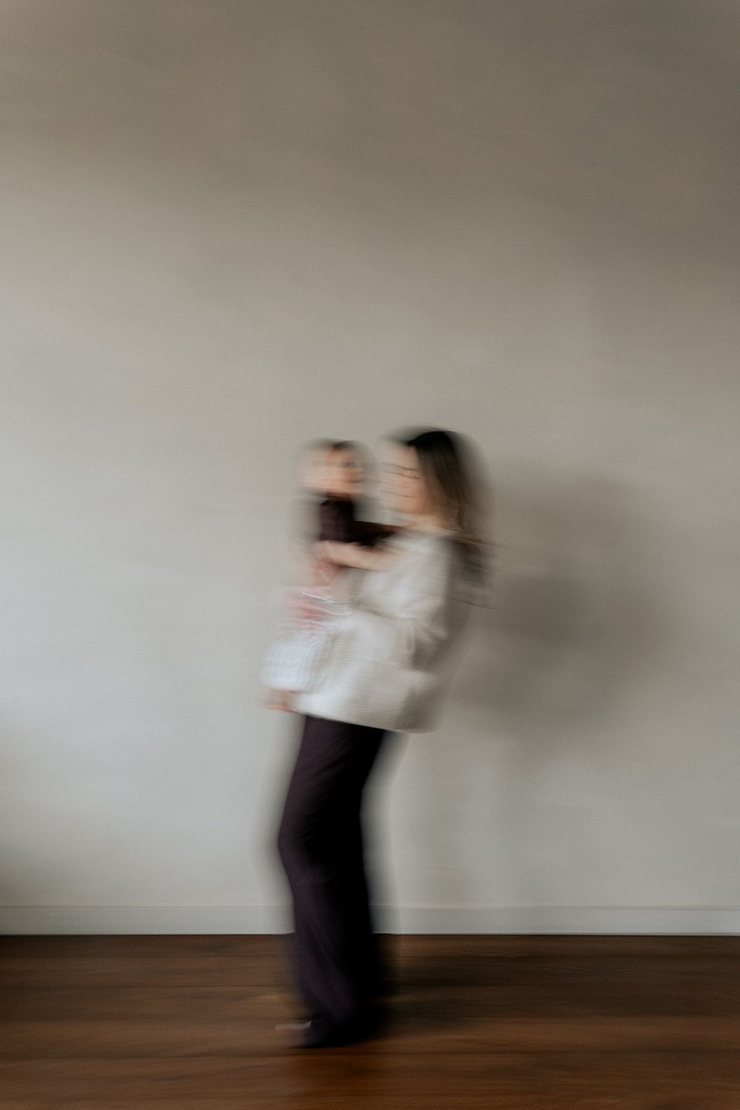 Motion blur photo of a mother holding her baby against a neutral wall background.