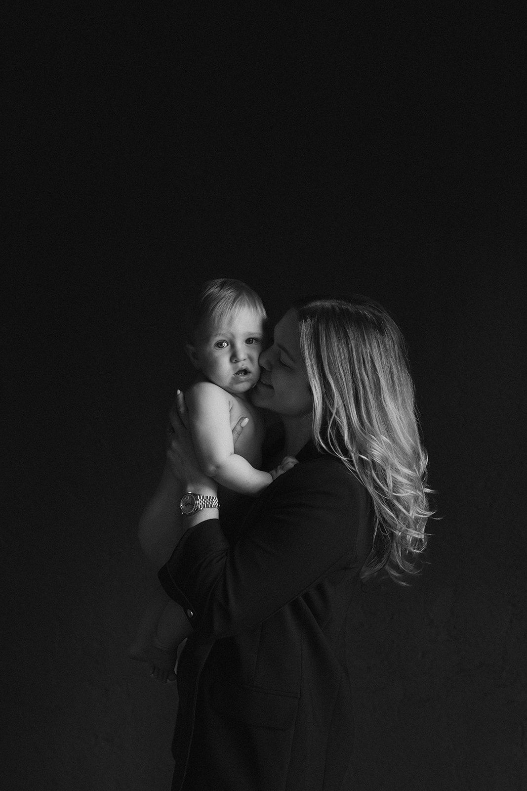 Black and white photo of a mother kissing her baby on the cheek while holding them close.