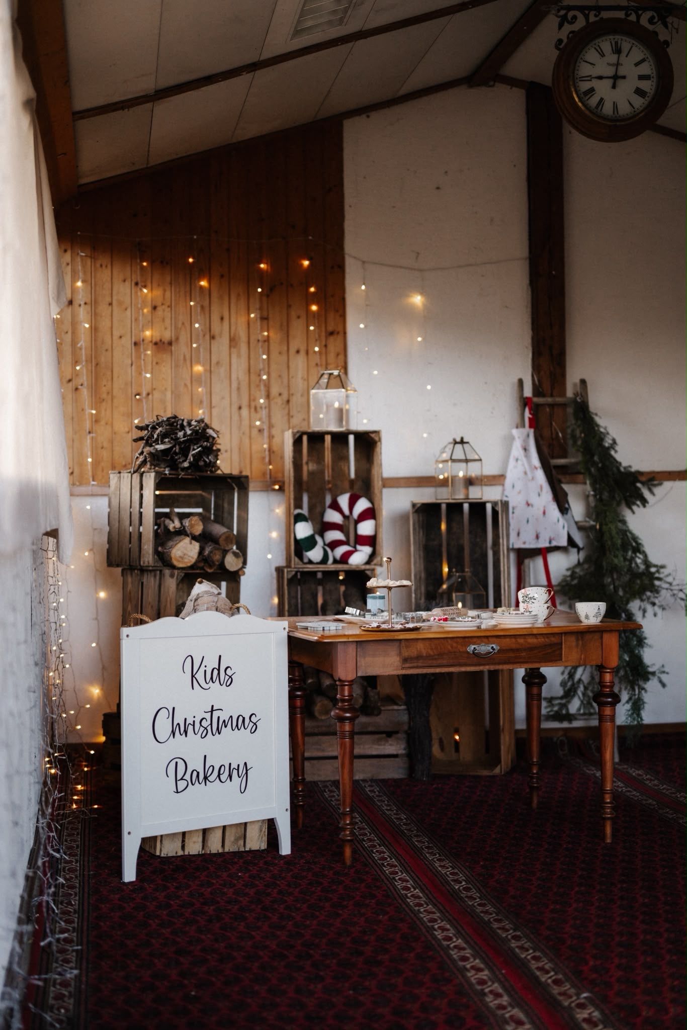 Cozy Kids Christmas Bakery station with fairy lights, wooden crates, candy canes, and festive decor in a rustic barn setting.