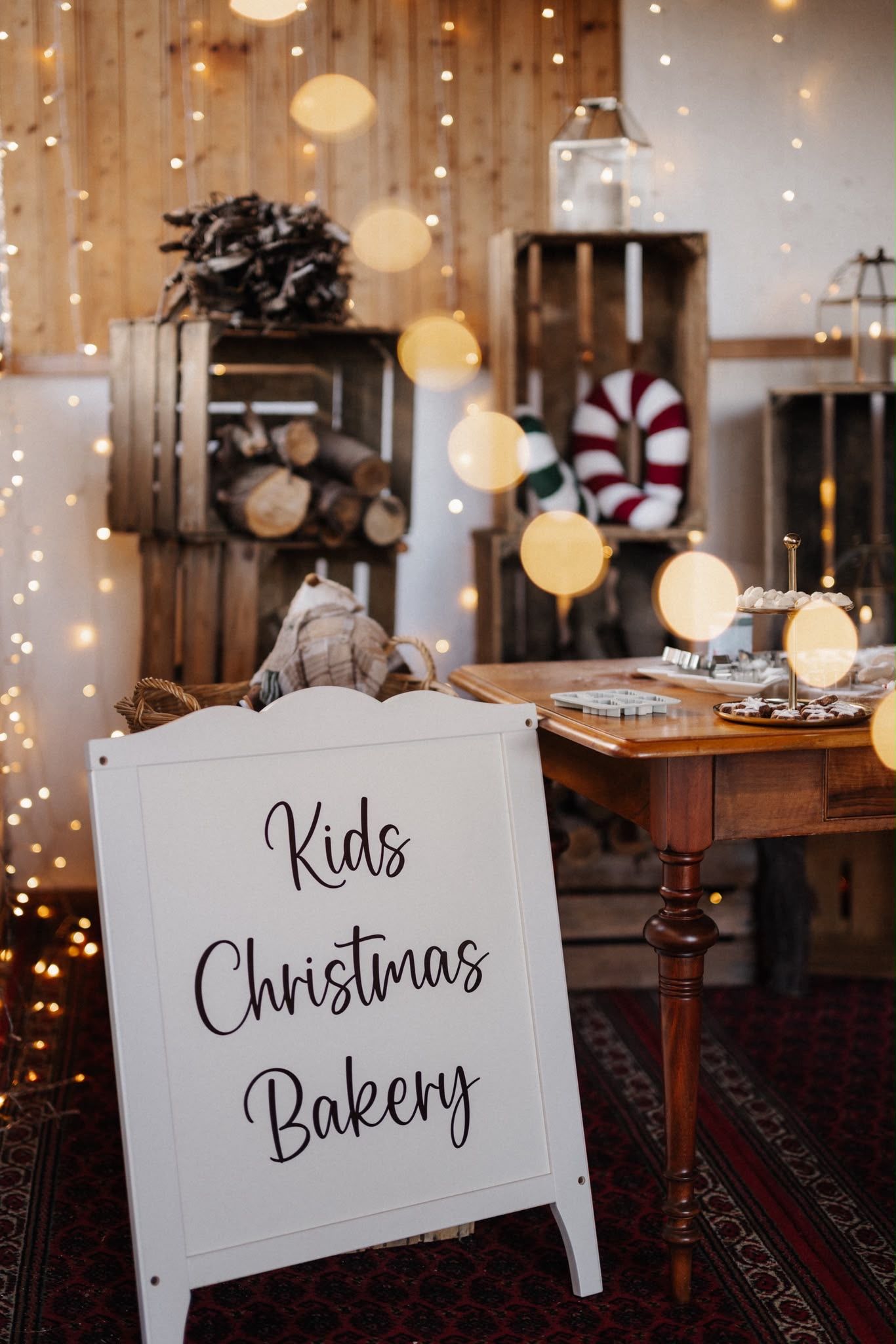 White Kids Christmas Bakery sign displayed in a festive holiday setting with warm fairy lights and wooden crates.