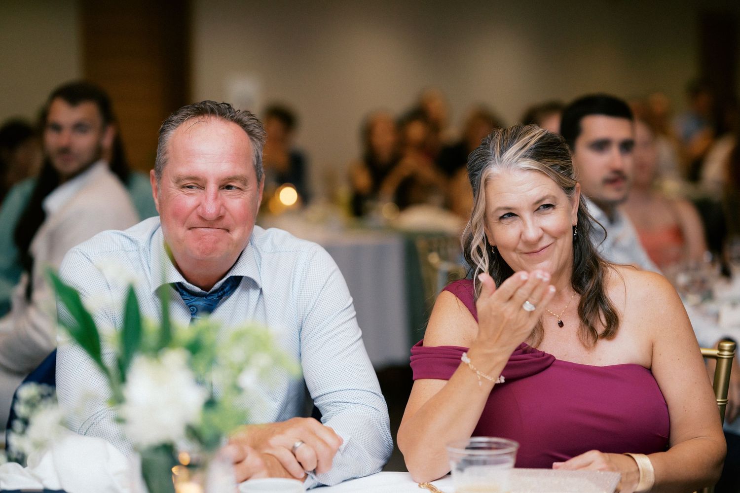 Smiling couple seated at wedding reception dinner table in elegant banquet hall.