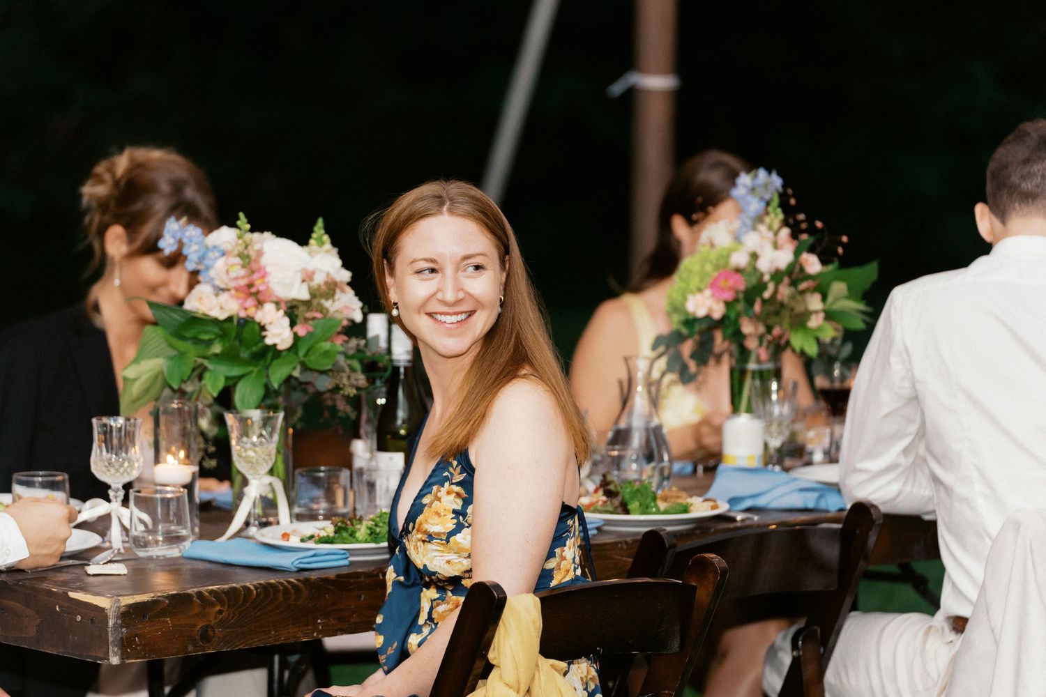 Wedding reception dinner table setup outdoors with floral centerpieces and glassware.