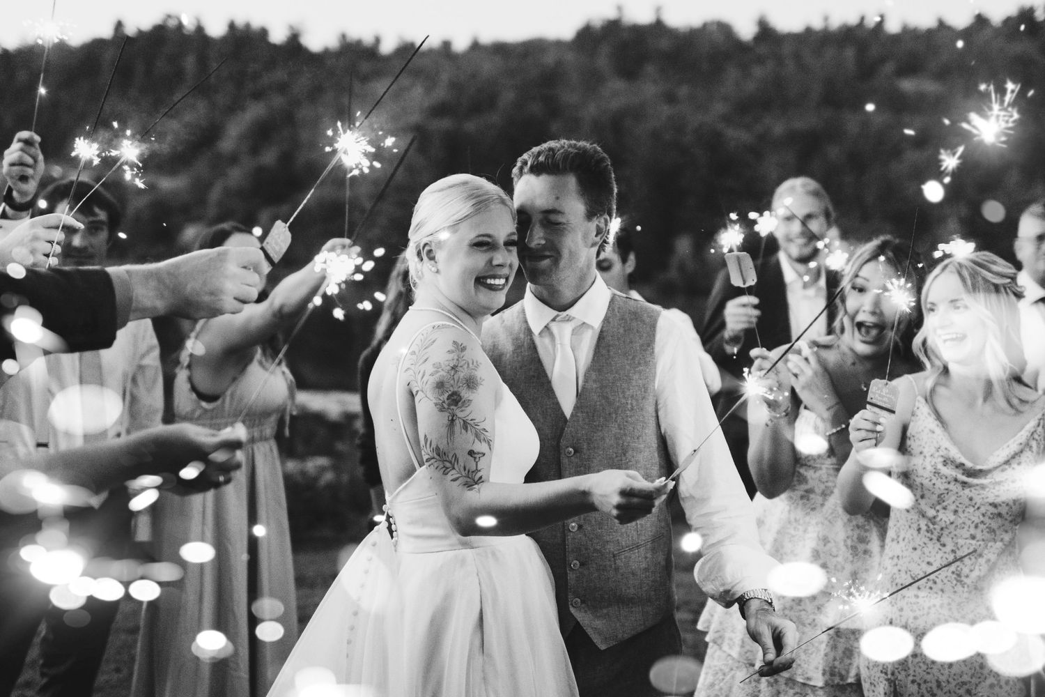 Black and white photo of a joyful wedding celebration with sparklers creating a magical nighttime atmosphere.