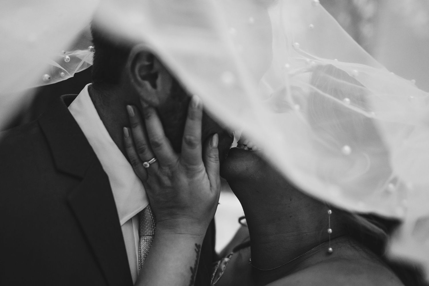 Black and white intimate wedding moment captured through delicate white veil during emotional ceremony.