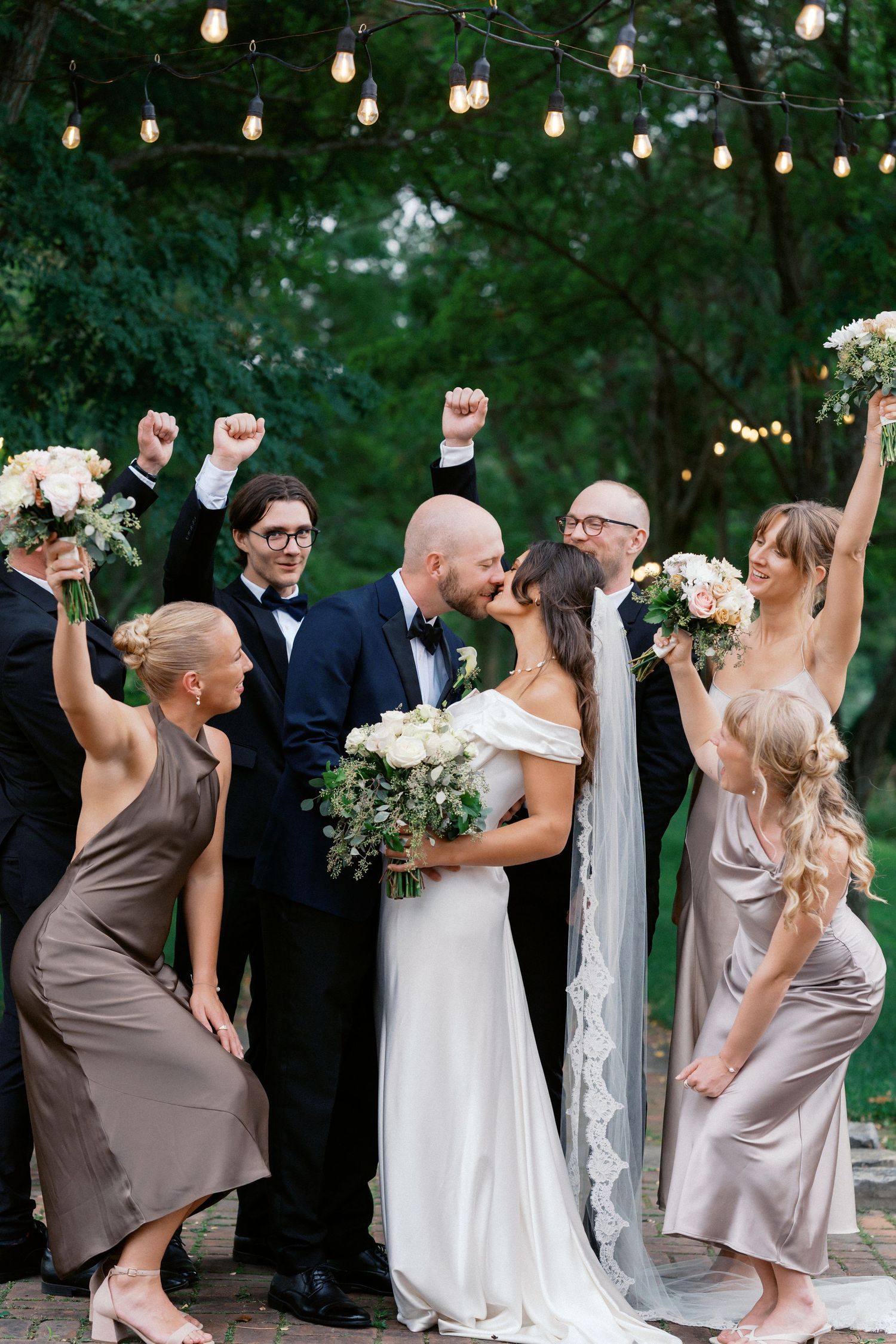 Wedding celebration with string lights and guests dancing joyfully in an outdoor garden setting.