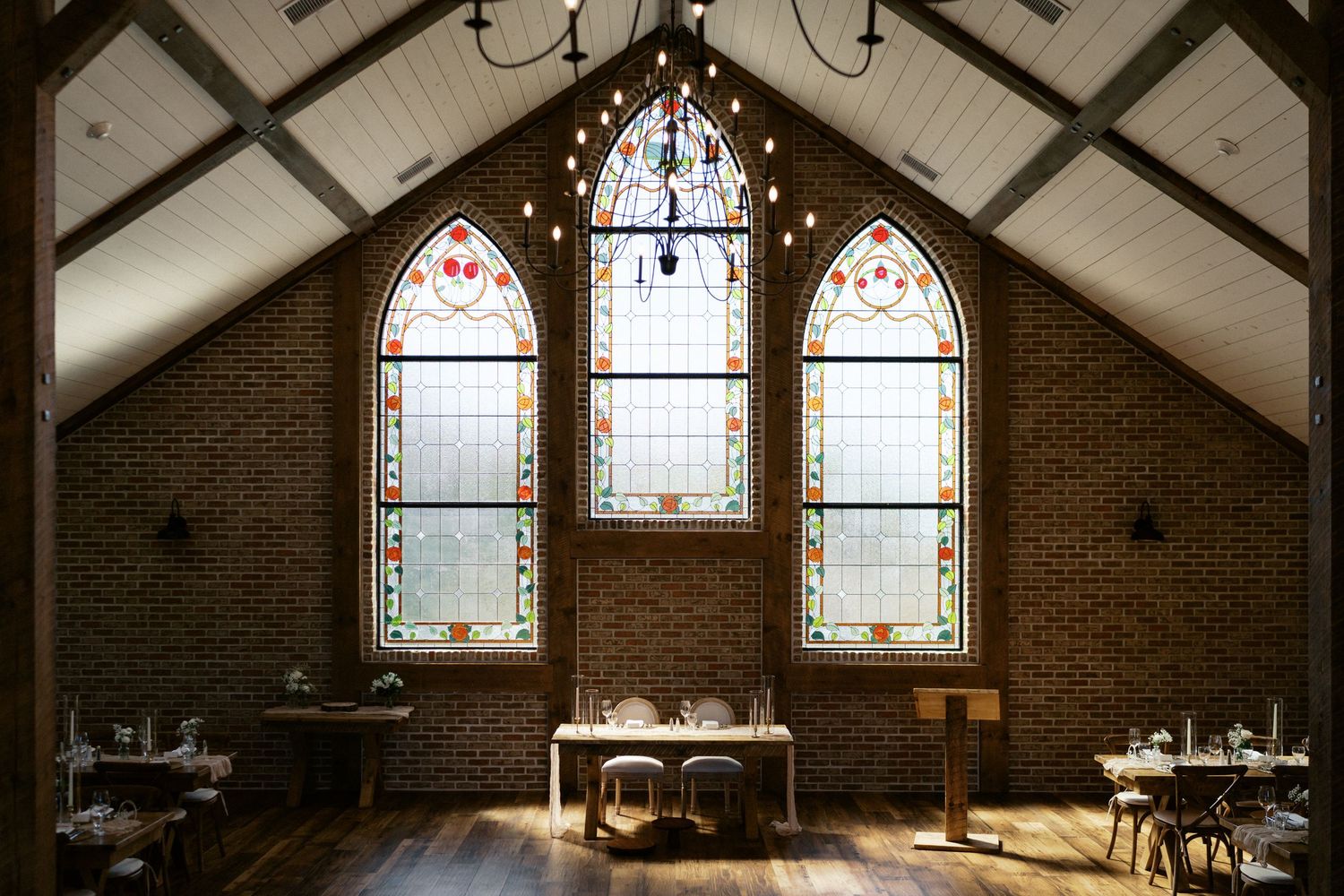 Stained glass windows in a brick chapel create a dramatic backdrop for a wedding ceremony.