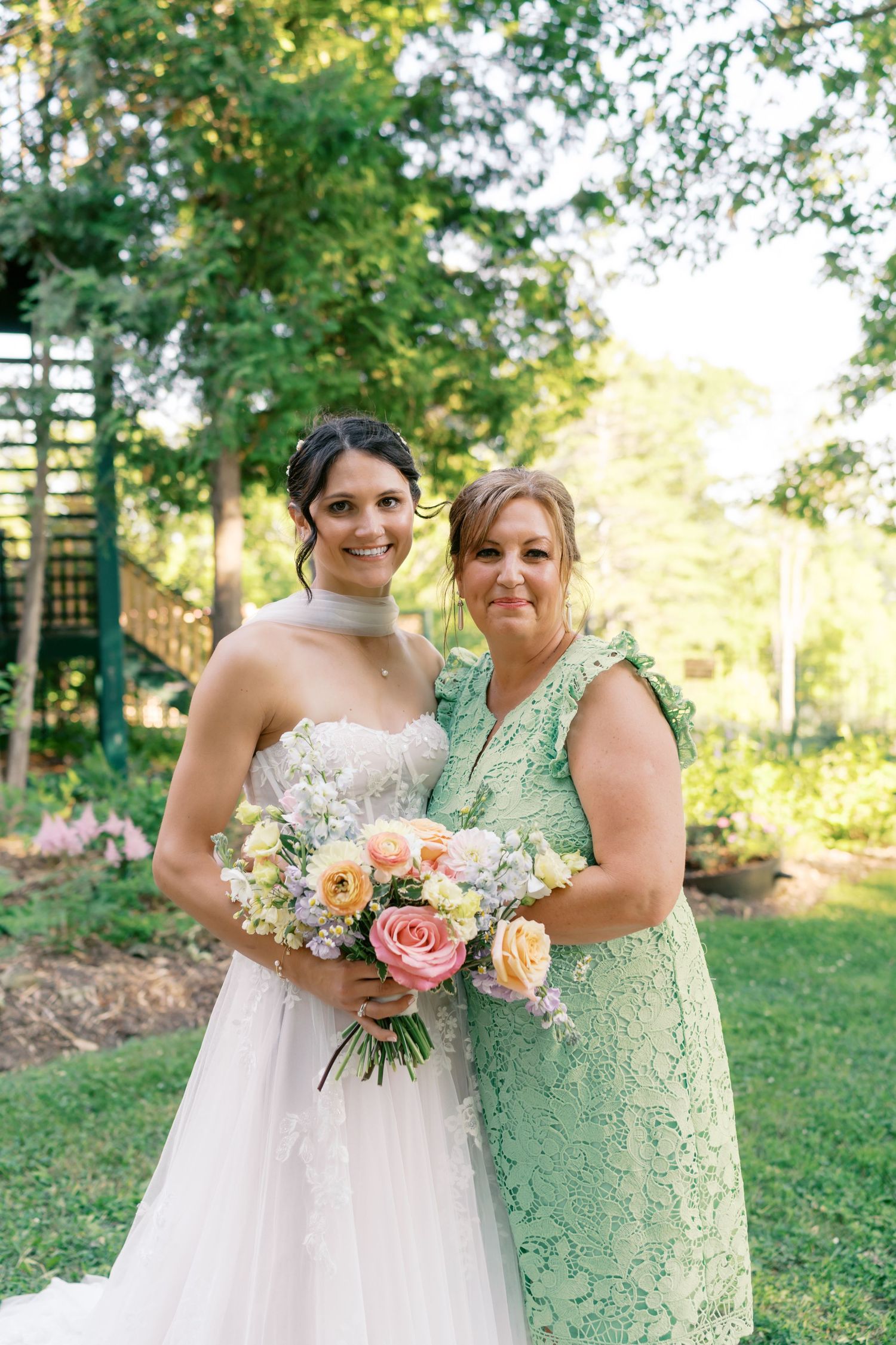 Wedding party members pose with peach and cream bouquets in garden setting.