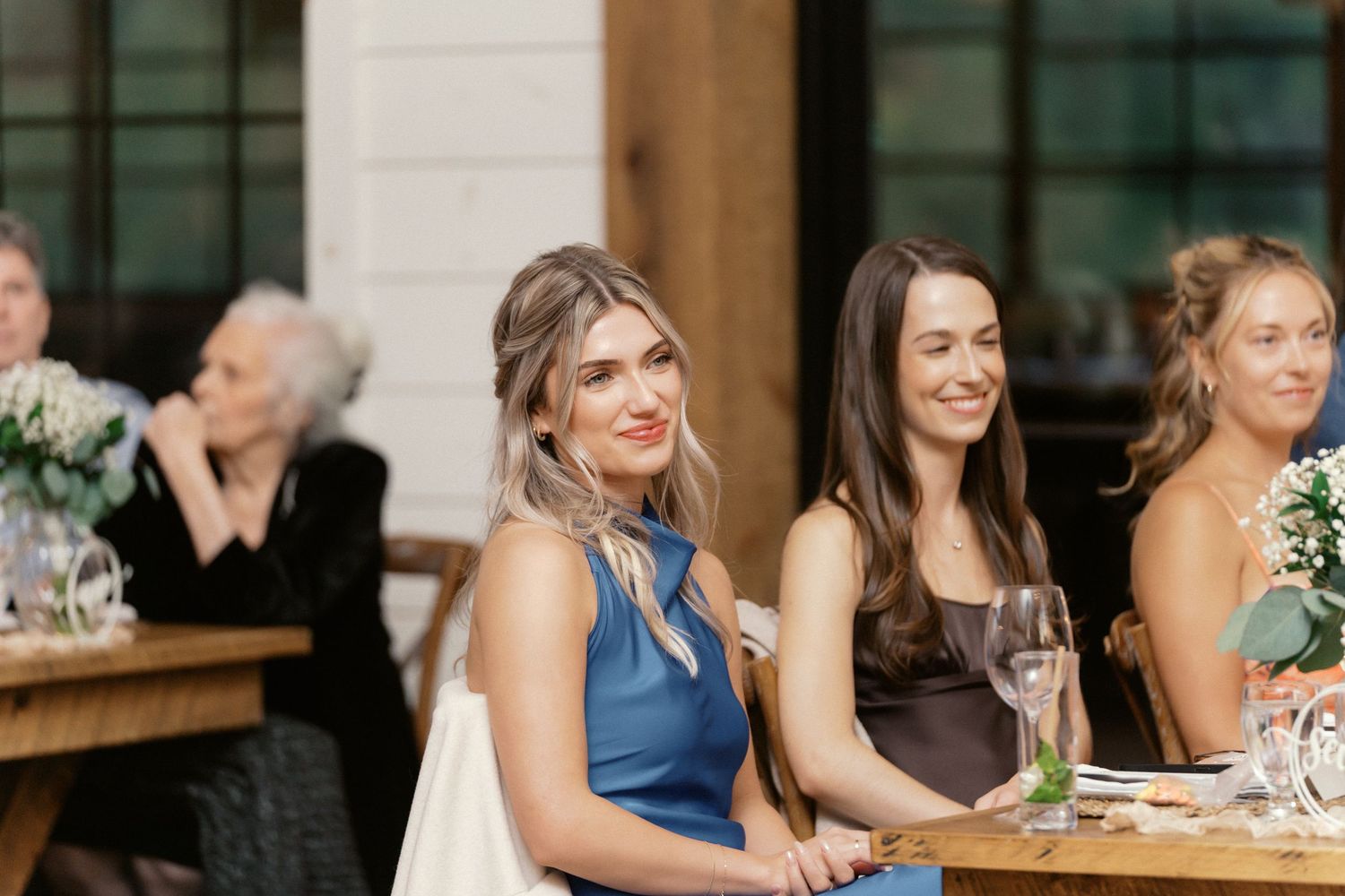 Wedding guests seated at outdoor reception tables smile and enjoy the celebration.