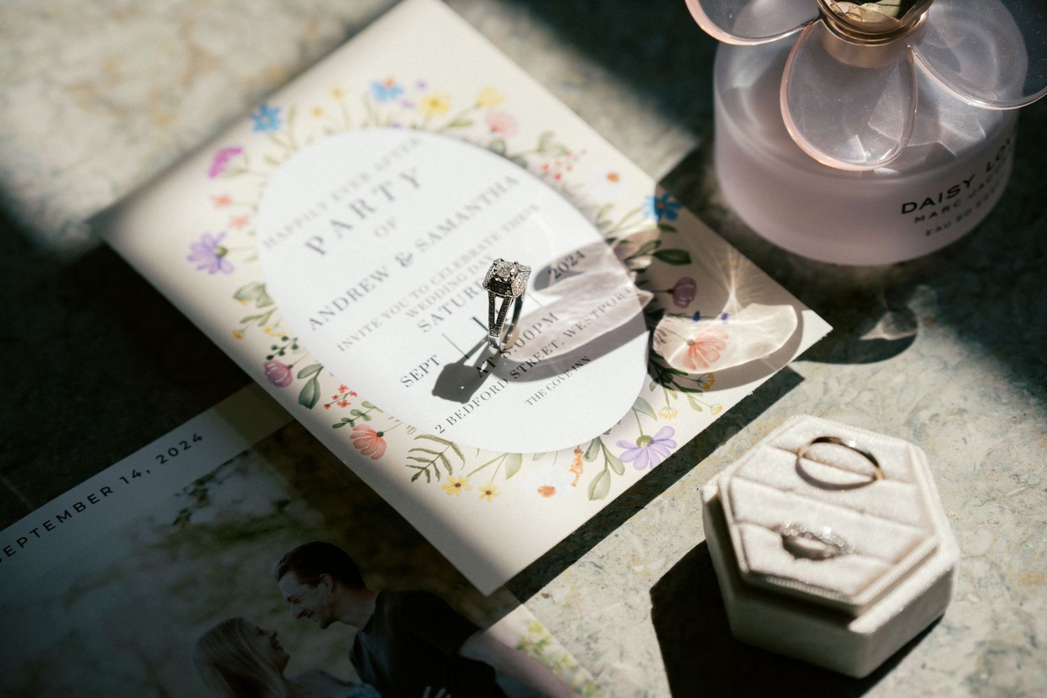 Wedding details flatlay with rings, invitation and perfume in natural light.