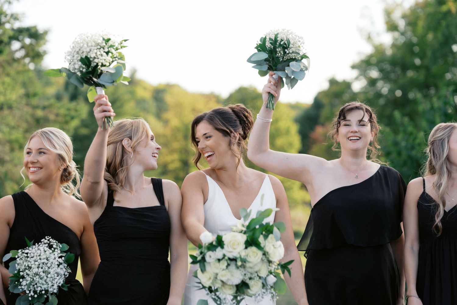 Wedding party members in black dresses holding white floral bouquets.