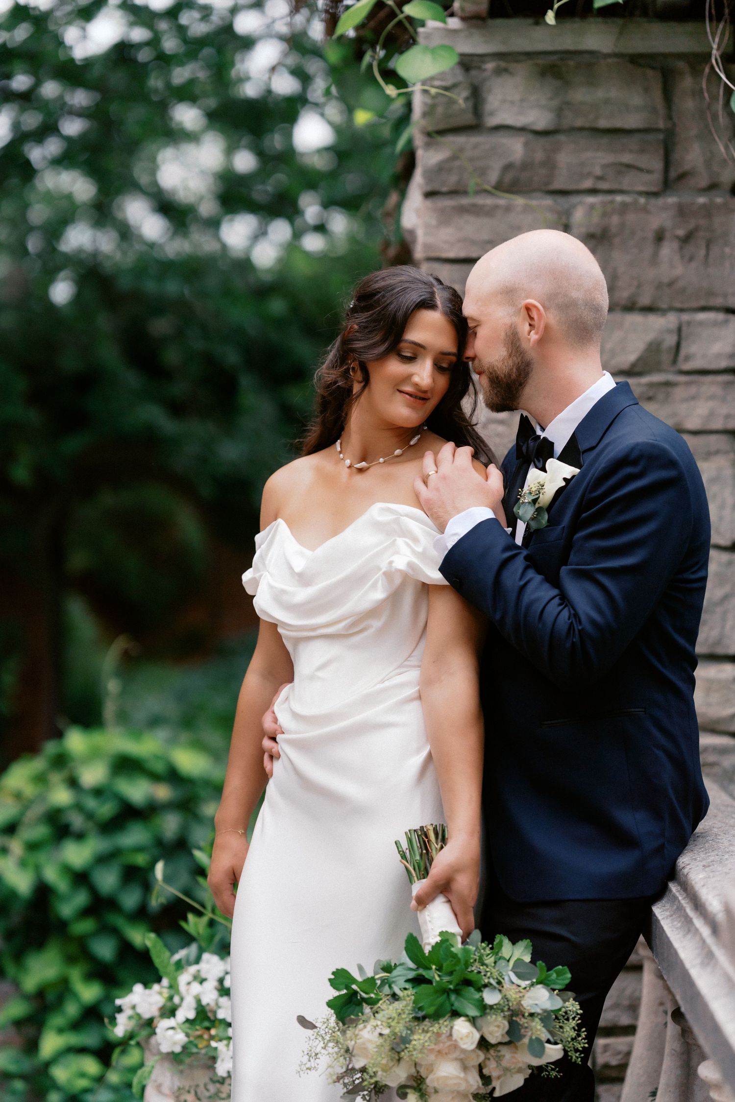 Romantic wedding portraits captured against a stone wall backdrop with natural greenery.