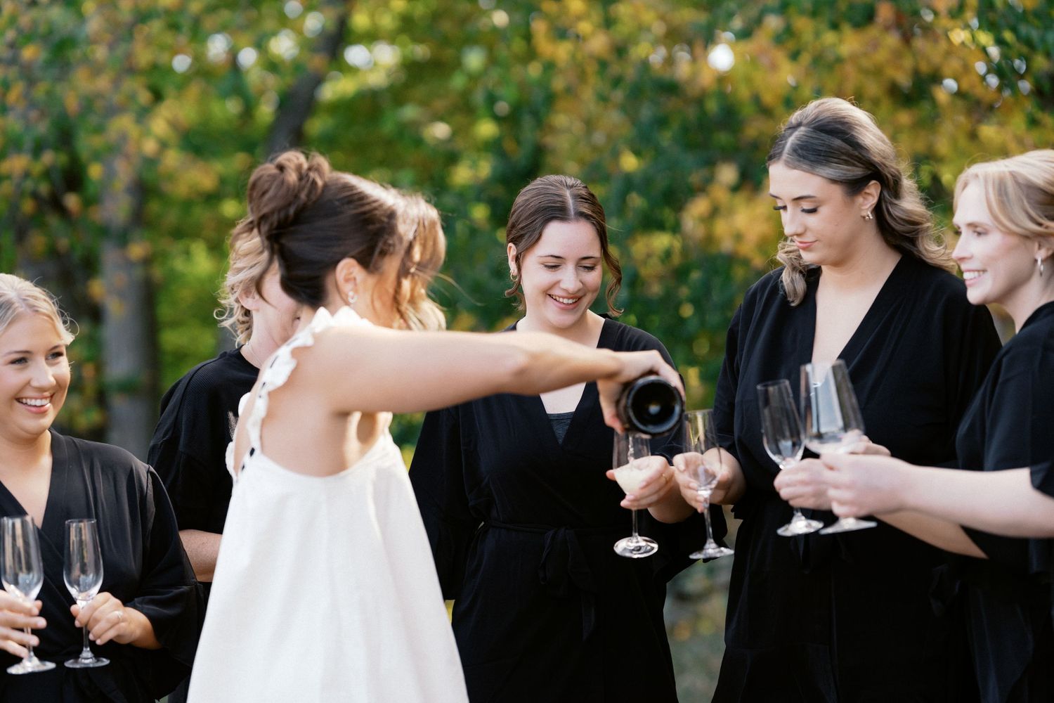 Wedding party in black and white attire toasting with champagne glasses outdoors.