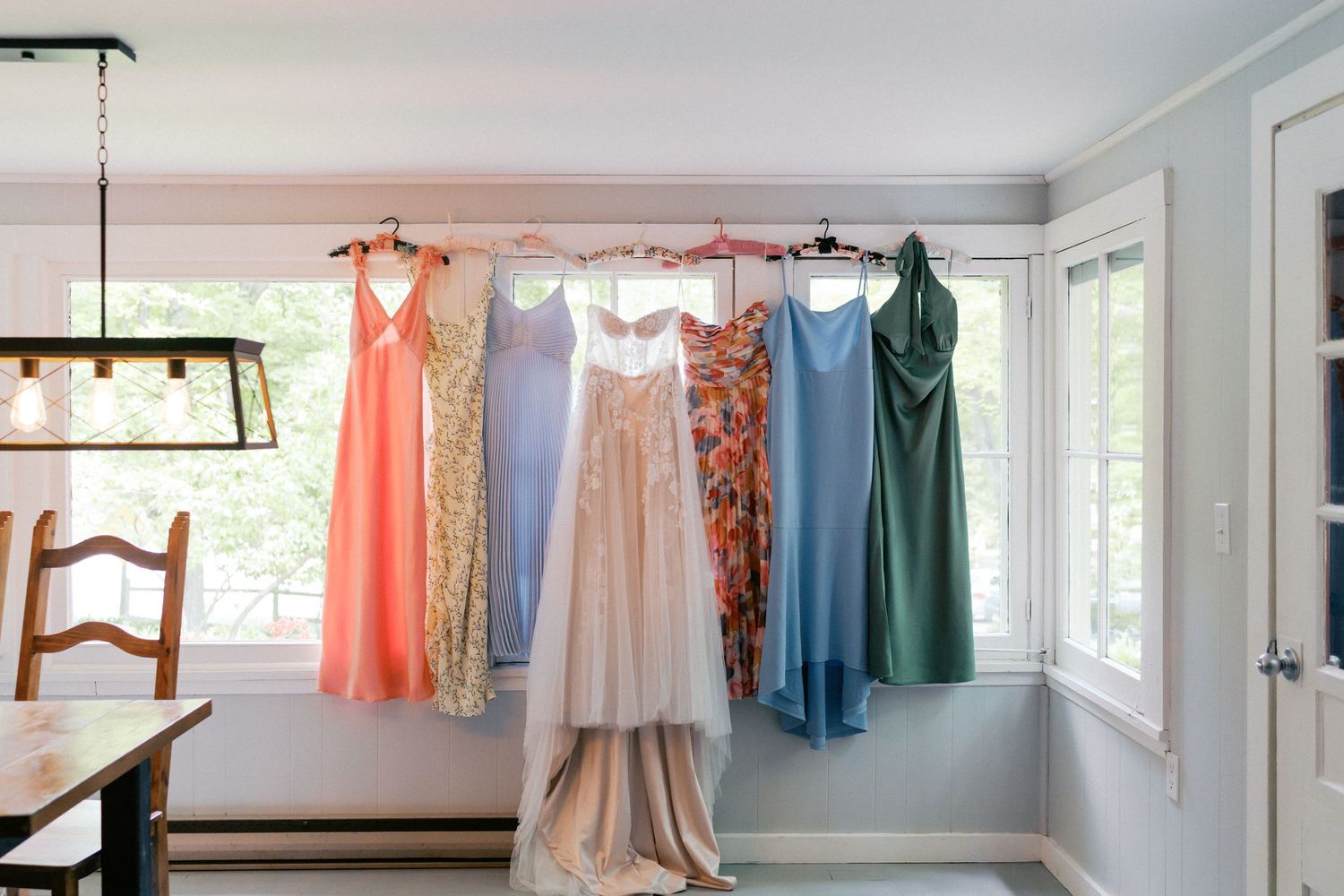 Elegant dresses and formal wear hanging on display in a bright, sunlit dressing room with white walls.