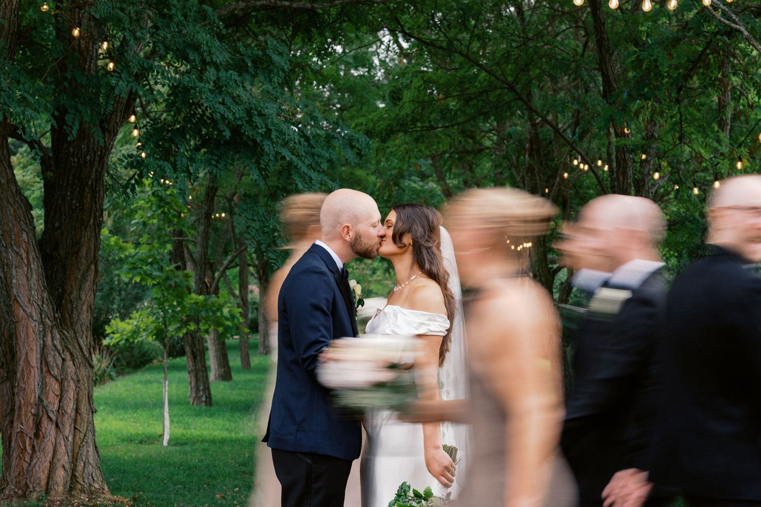 Wedding ceremony moment captured with motion blur of guests walking past in an outdoor garden setting.