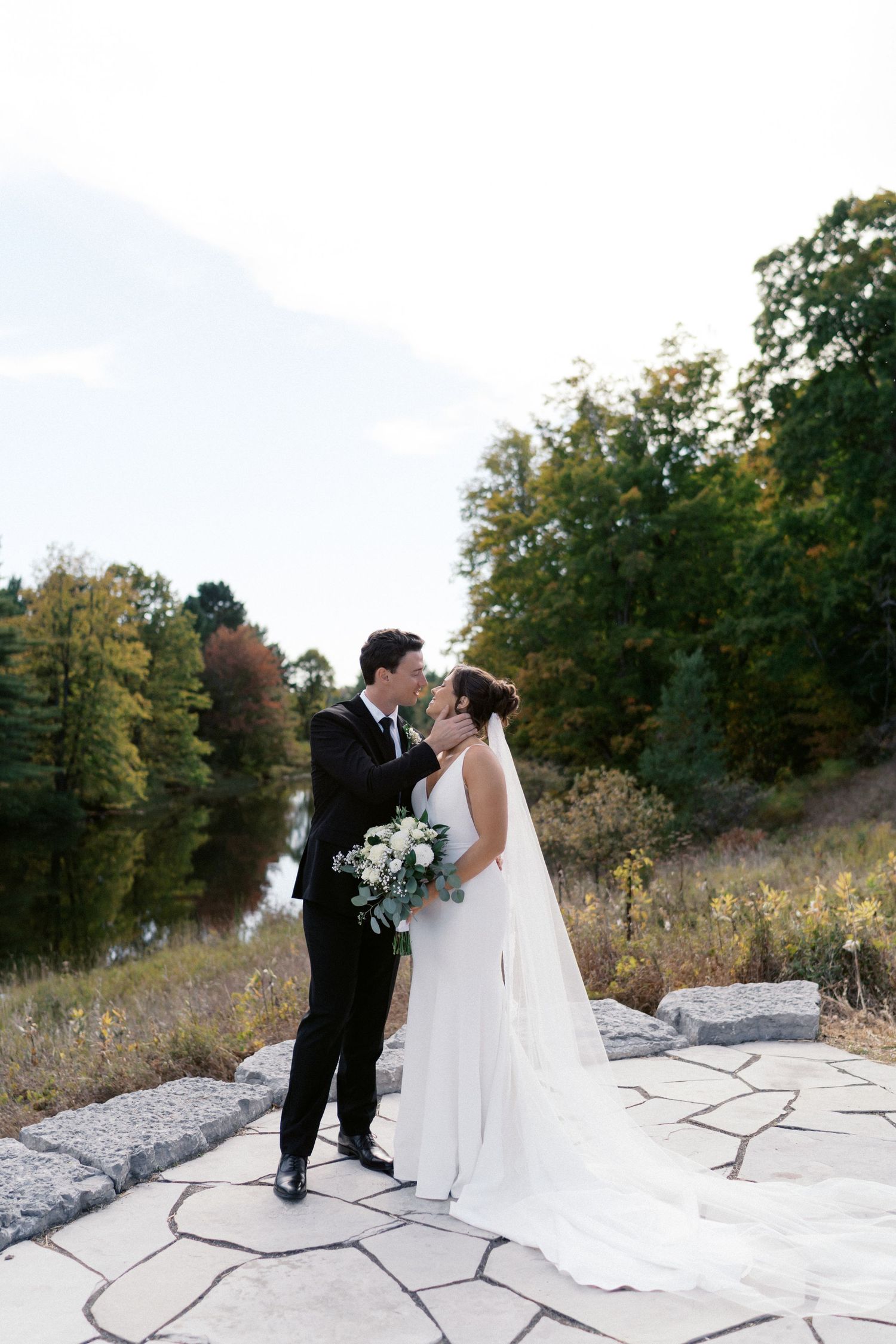 Wedding couple sharing romantic moment on stone pathway surrounded by autumn foliage.