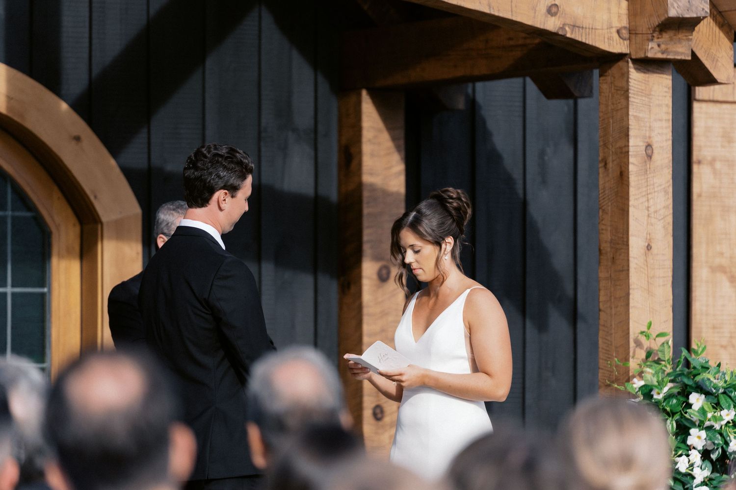 Wedding ceremony taking place under a wooden pergola with decorative floral arrangements.