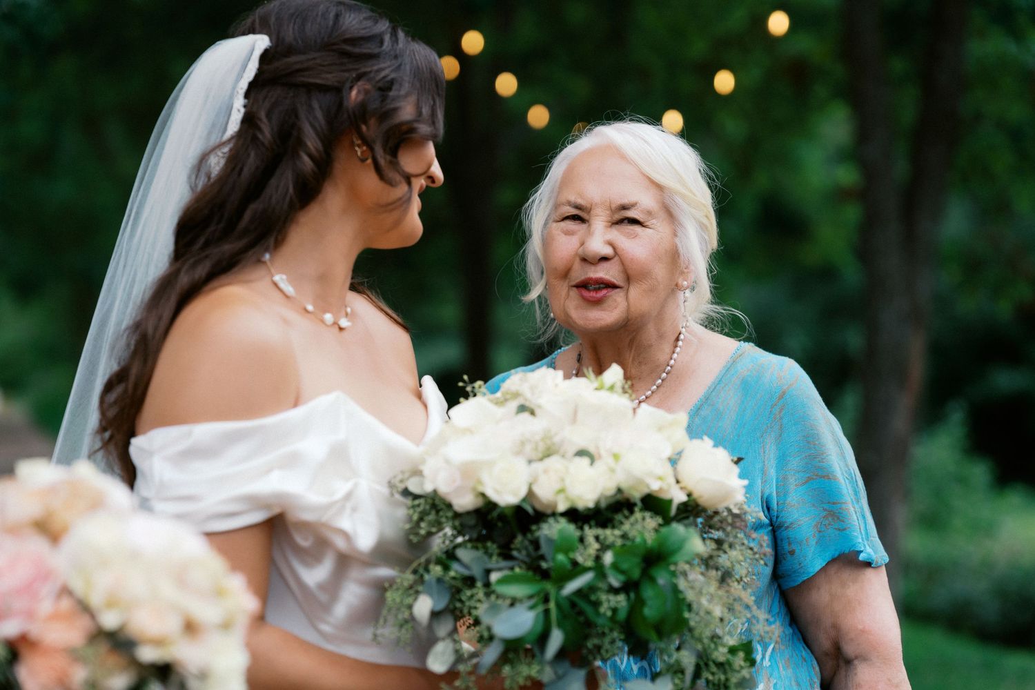 Wedding guests share emotional moments during an outdoor celebration with greenery in the background.