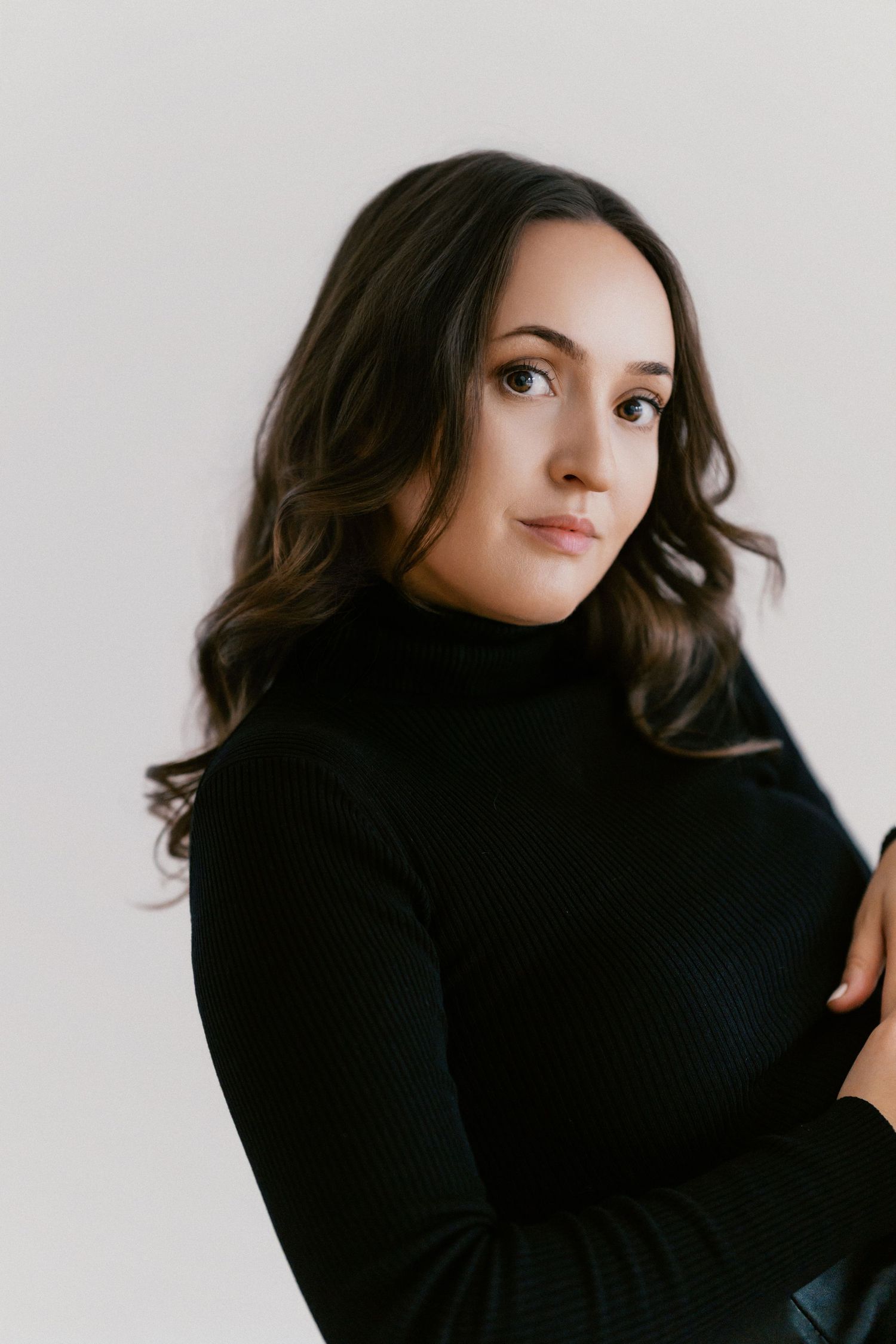 Studio portrait showing dark wavy hair and black turtleneck sweater against white backdrop.