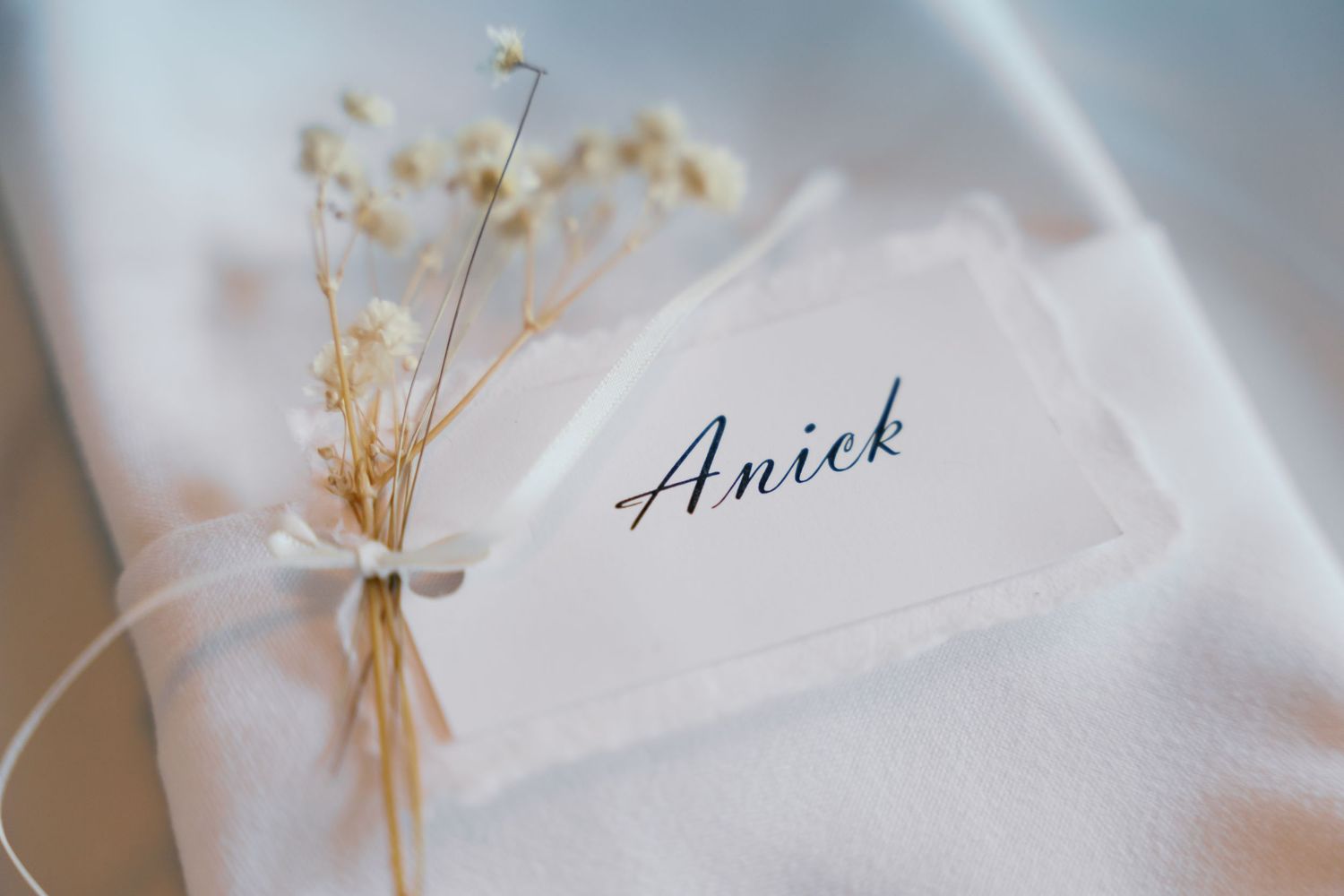 White linen napkins with delicate name cards arranged for an elegant wedding table setting.