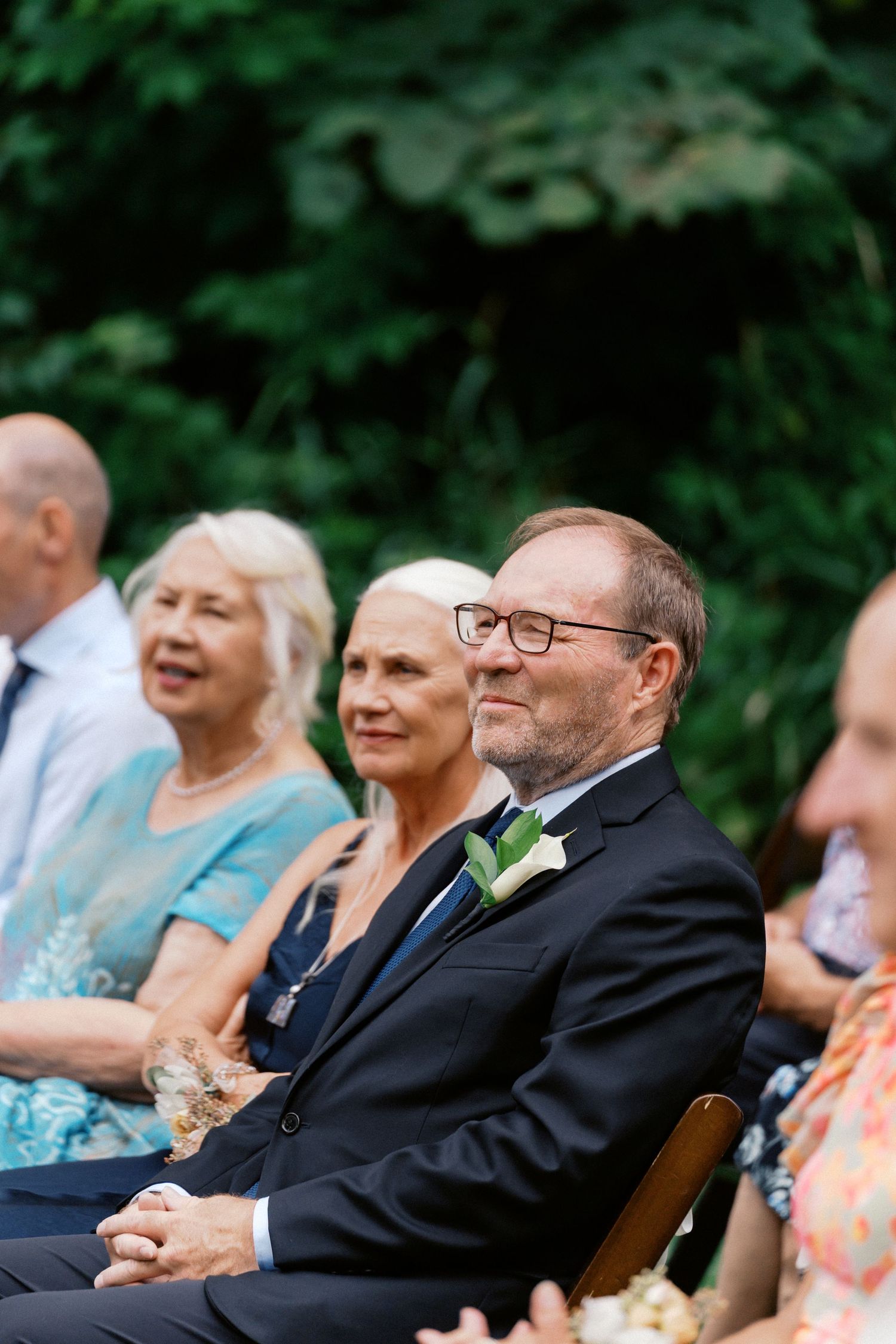 Wedding guests seated outdoors smile and watch the ceremony unfold.