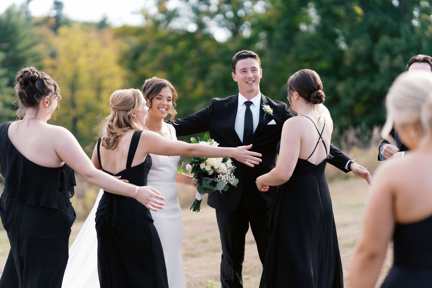 Bridal party in formal attire sharing joyful moments outdoors.