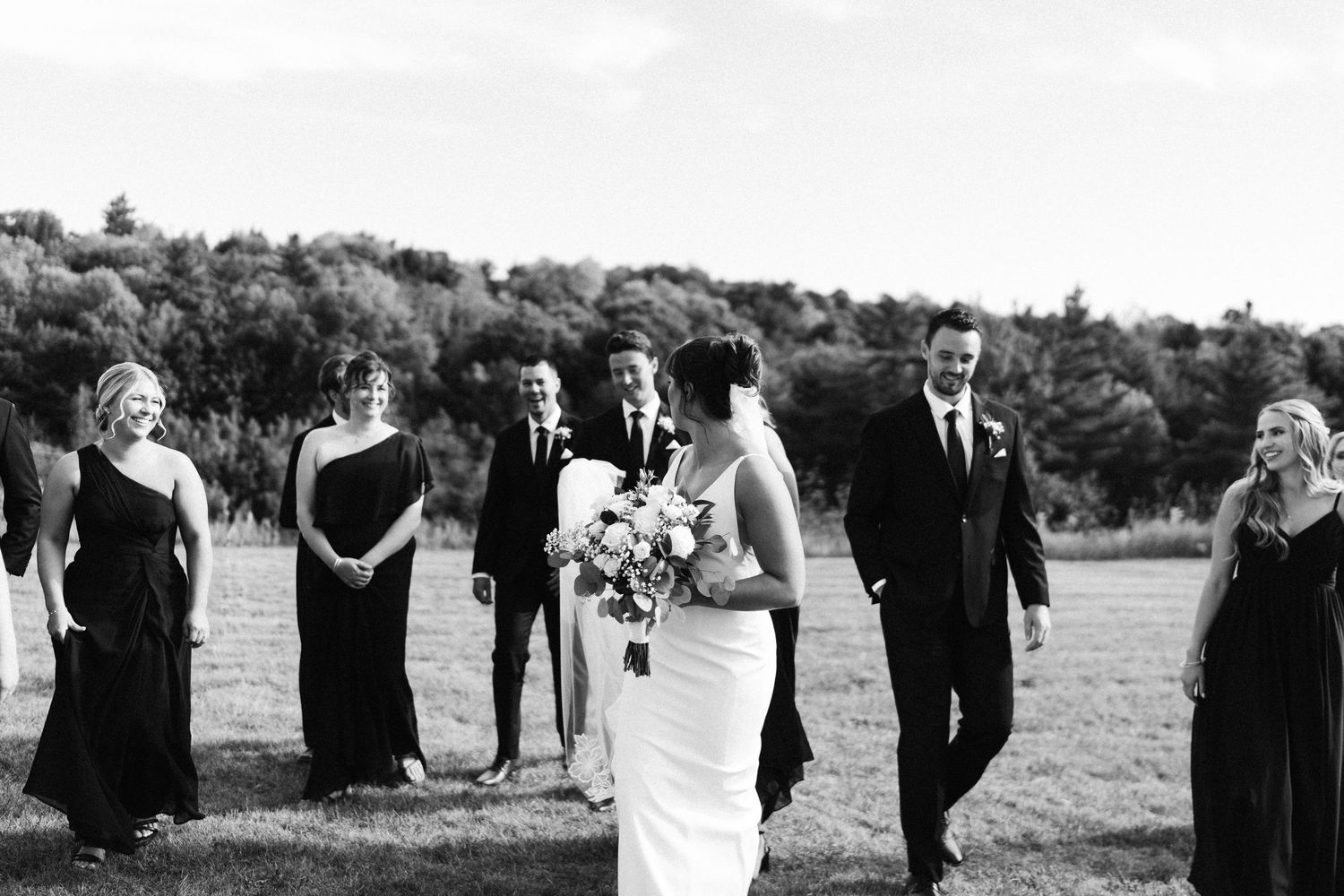 Wedding ceremony guests standing outdoors with scenic countryside views in the background.