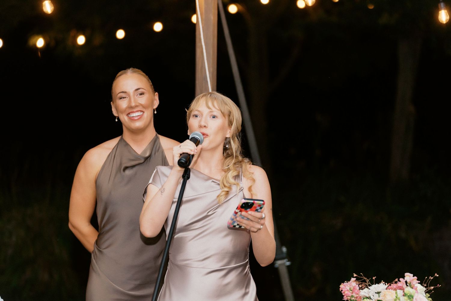 Evening celebration under string lights with speakers sharing joyful moments.